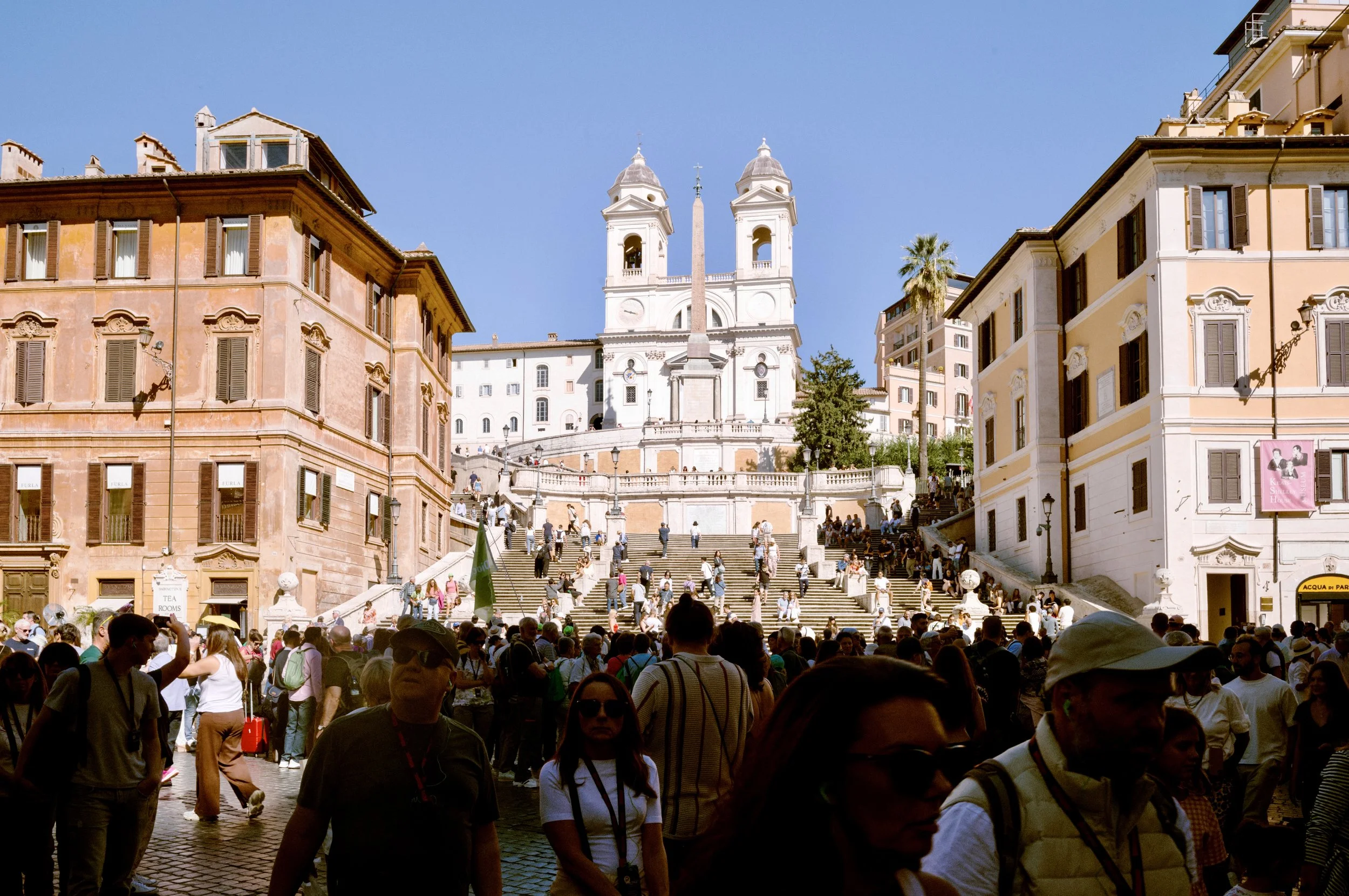 Crowds sitting on the Spanish Steps in Rome beneath Trinità dei Monti church on a bright afternoon.