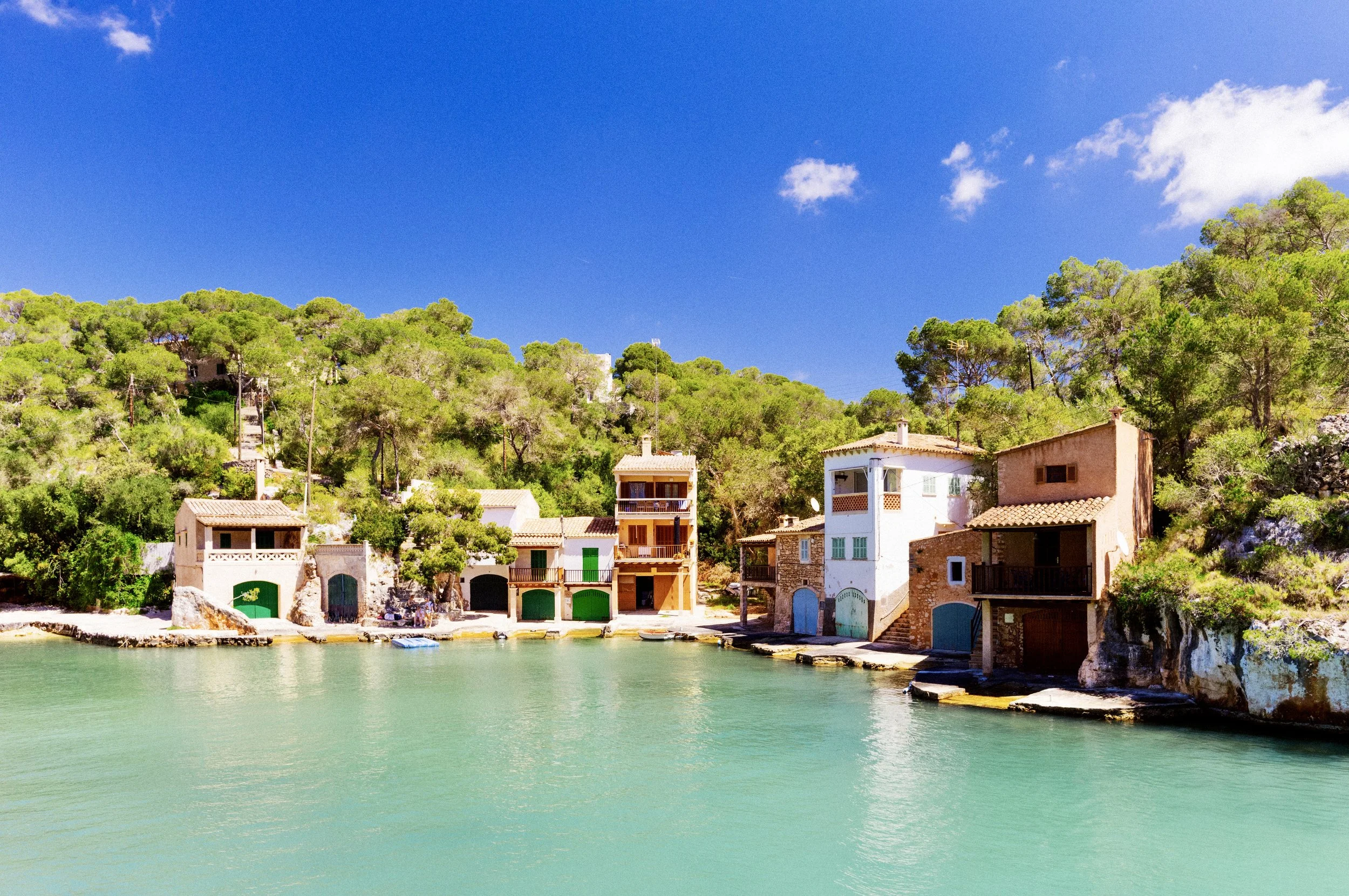 Stone boat houses with coloured doors lining a turquoise cove at Cala Figuera, Mallorca