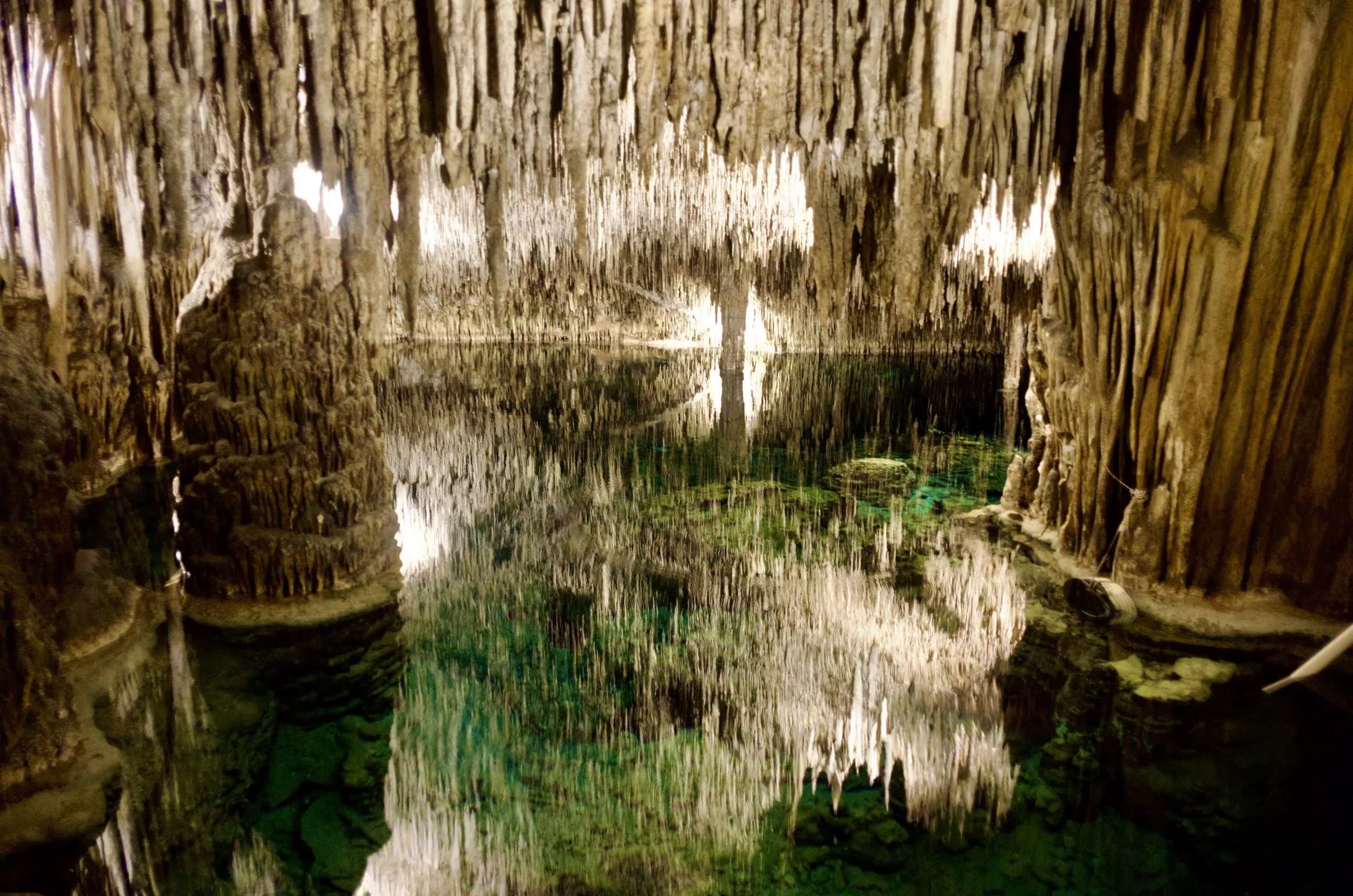Stalactites reflected in the still emerald water of an underground cave lake in Mallorca