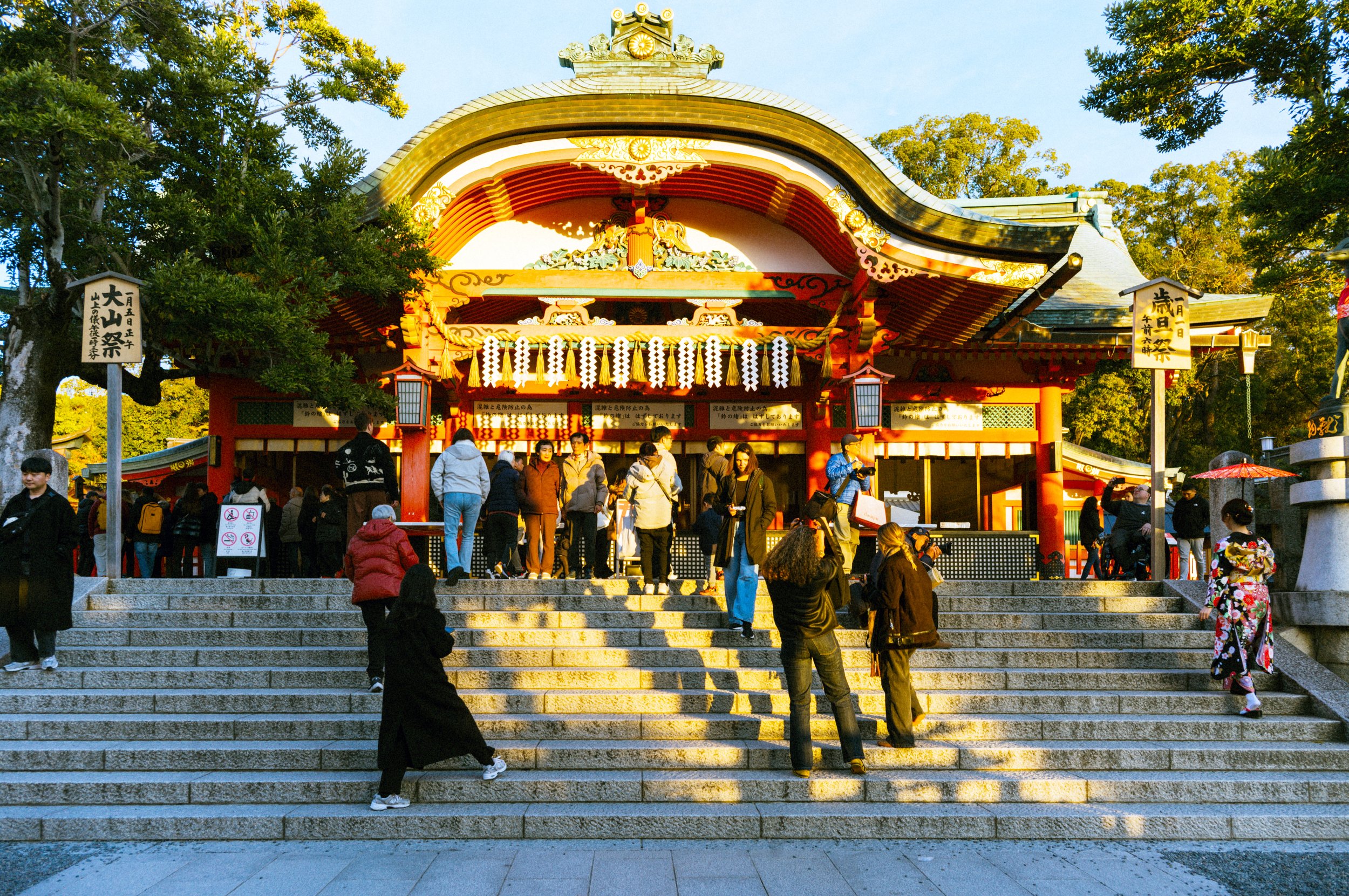 Visitors walking up the stone steps towards the bright vermilion shrine buildings at Fushimi Inari Taisha in Kyoto, Japan.