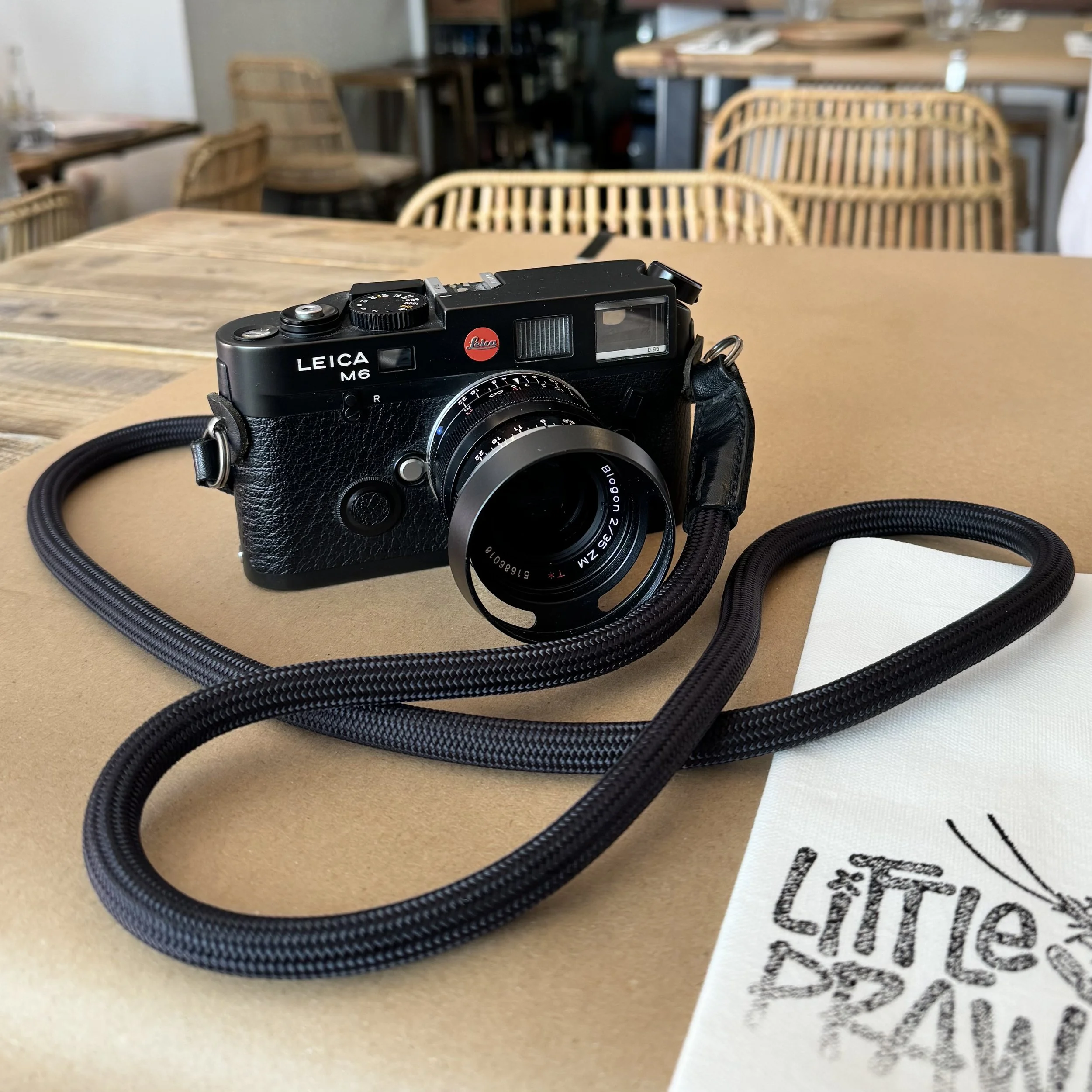 Leica M6 TTL .85 rangefinder film camera resting on a wooden table at a Cornwall restaurant, camera strap coiled beside it
