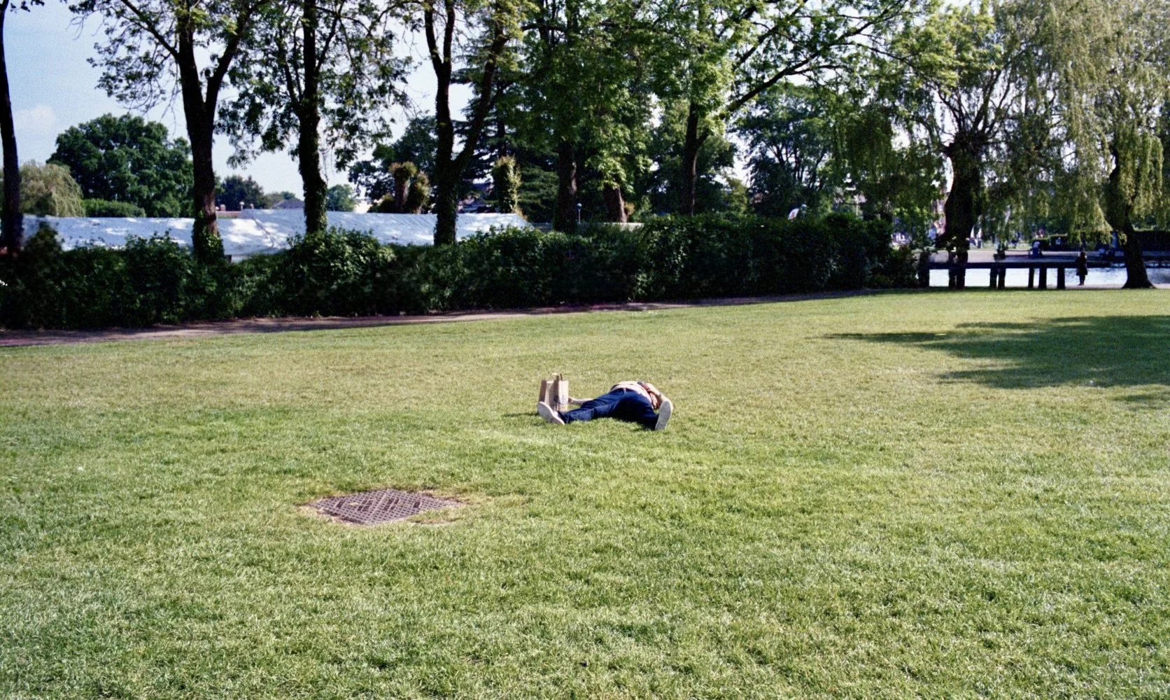 A man sleeping in the middle of a park with a shopping bag beside him, captured as an unexpected street photography moment on colour film.