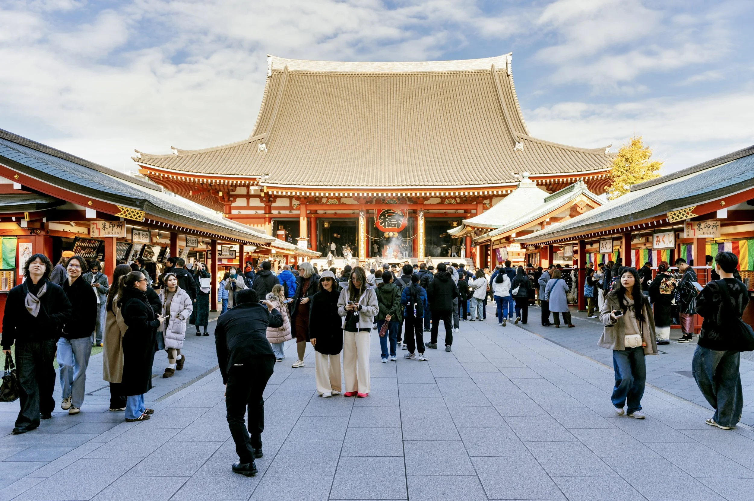 Visitors walking through Nakamise Shopping Street toward the main hall of Sensō-ji Temple in Asakusa, Tokyo, under a bright winter sky.