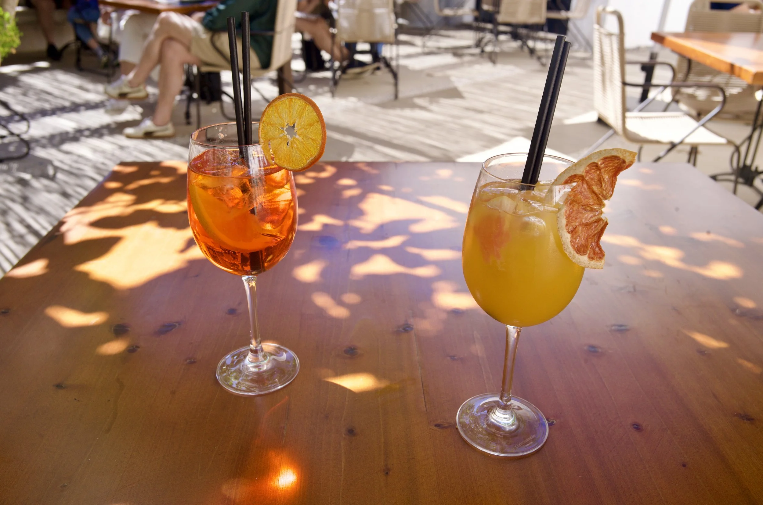 Two citrus cocktails with dried orange and grapefruit garnishes on a sunlit café table in Mallorca