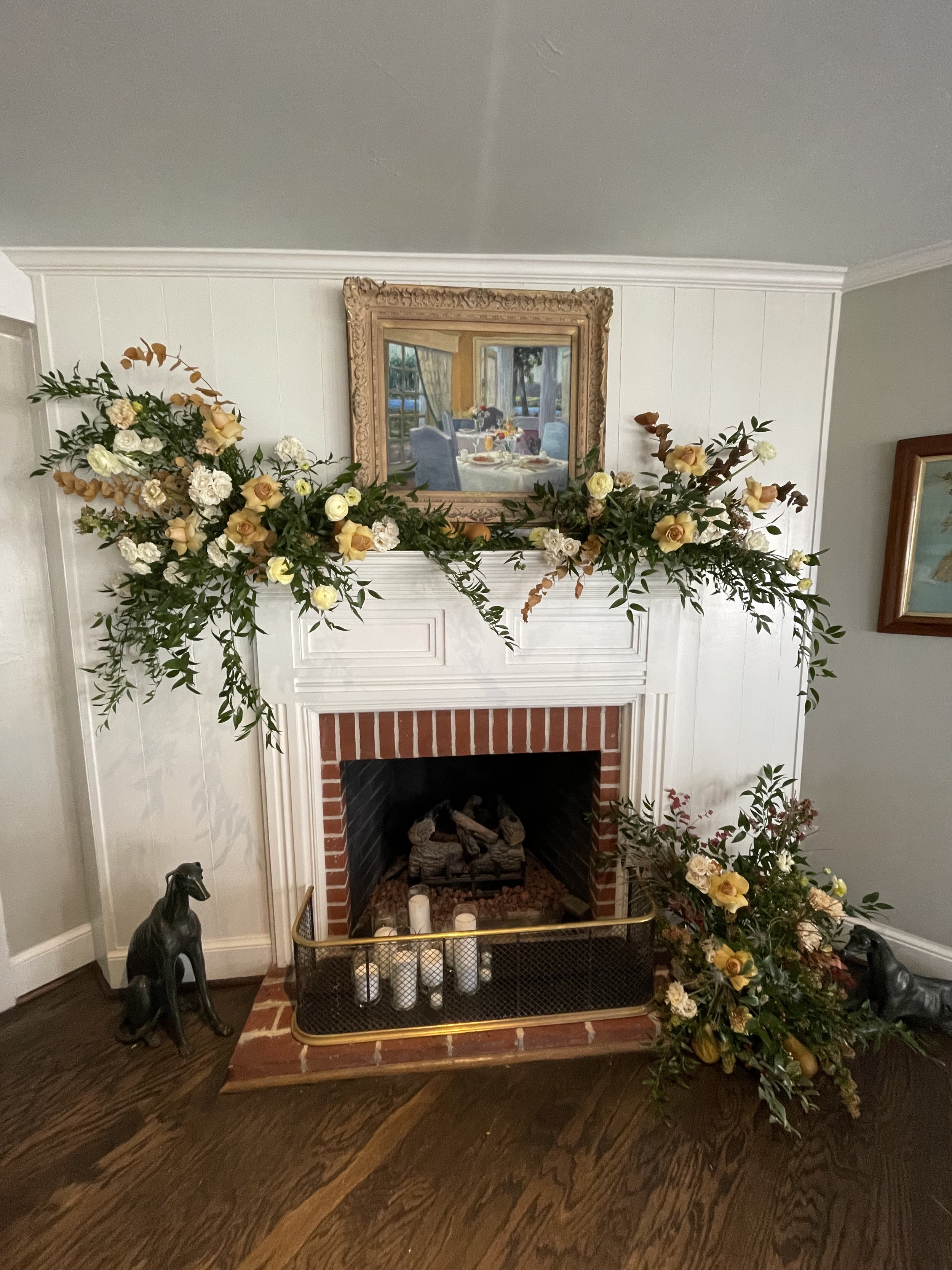 Decorated fireplace with floral garland, candles, and artwork in a living room.
