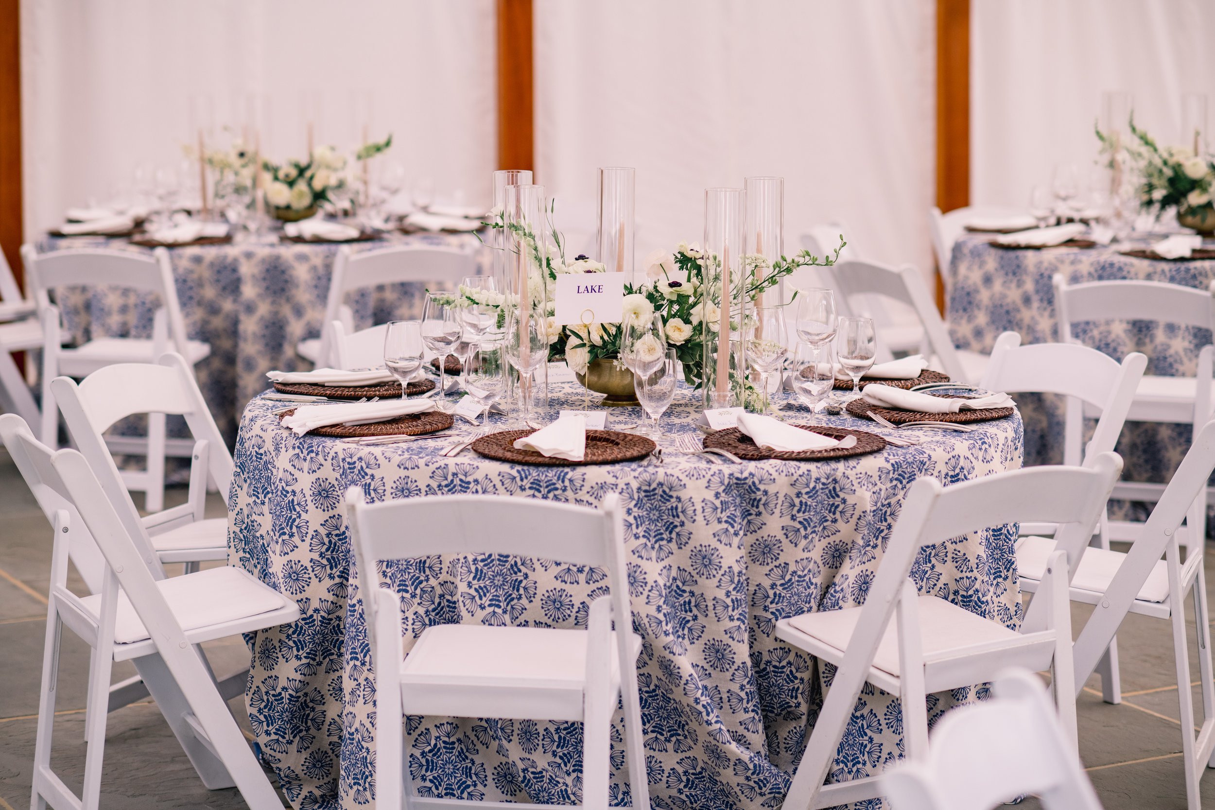 Round banquet table set with white folding chairs, floral centerpiece, glassware, napkins, and placemats, decorated for an event.