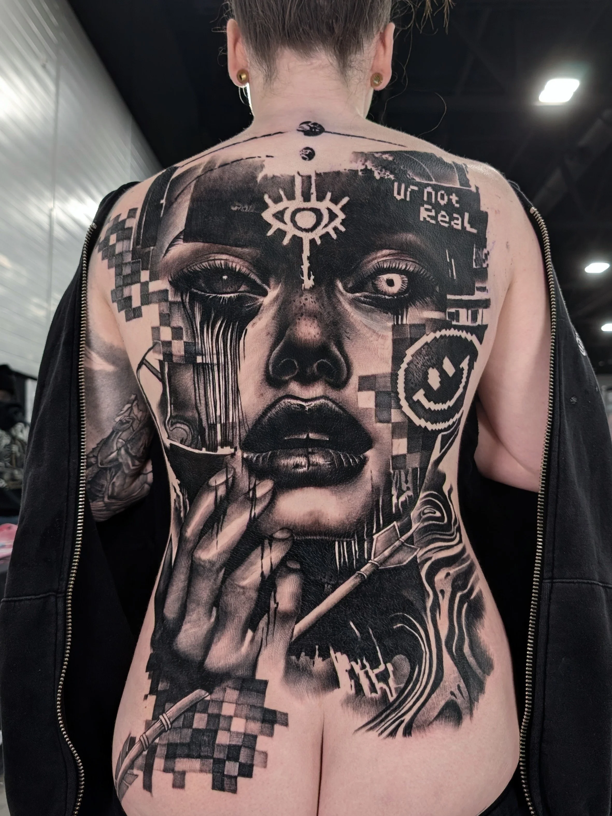 Full black and grey backpiece of a woman's face and hand with an arrow piercing it