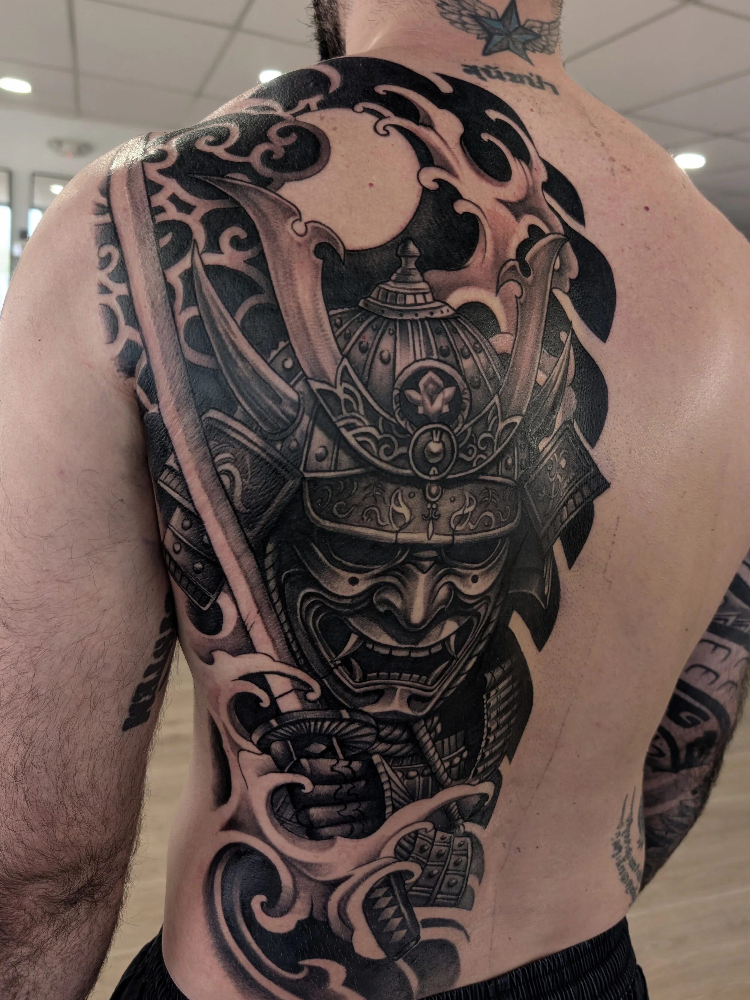 Black and grey half backpiece tattoo of a samurai holding a sword