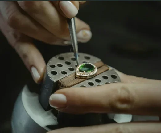 Jeweler setting a green emerald gemstone into a gold pendant surrounded by diamonds, representing Layaz’s hallmark of handcrafted precision and luxury craftsmanship.