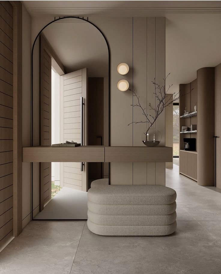 Modern entryway with a beige upholstered bench, a decorative vase with bare branches, and a small floating console table. The door is open, revealing a bright exterior, and there are two round wall lights on the wall.