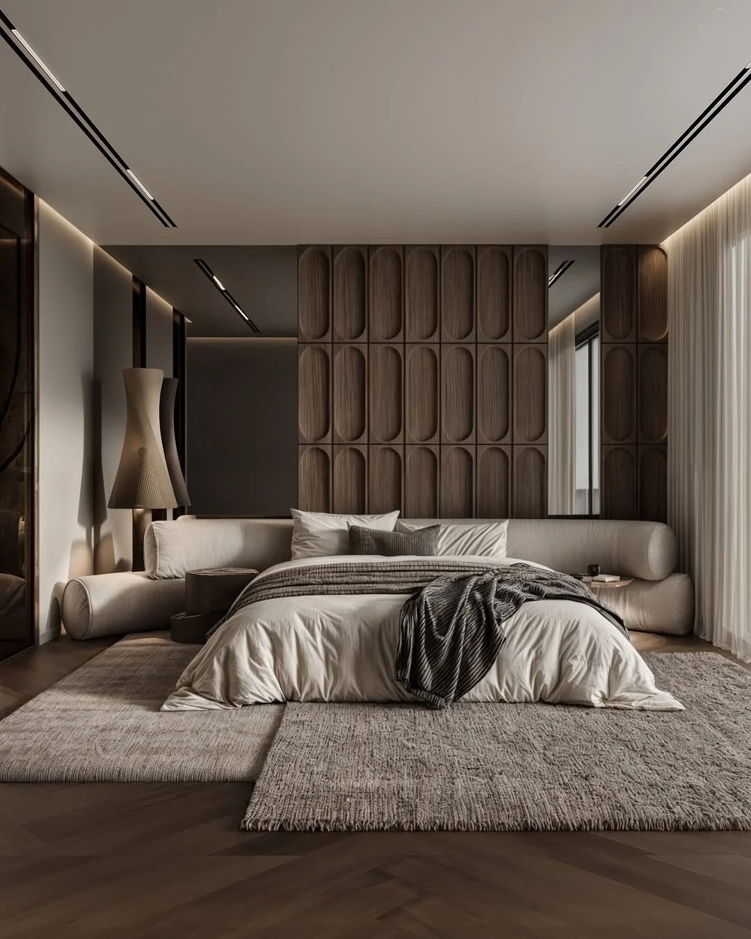 A modern bedroom with a low, white bed surrounded by a beige area rug, a beige long sofa against the wall, a tall beige floor lamp, and a wooden accent wall with a pattern.