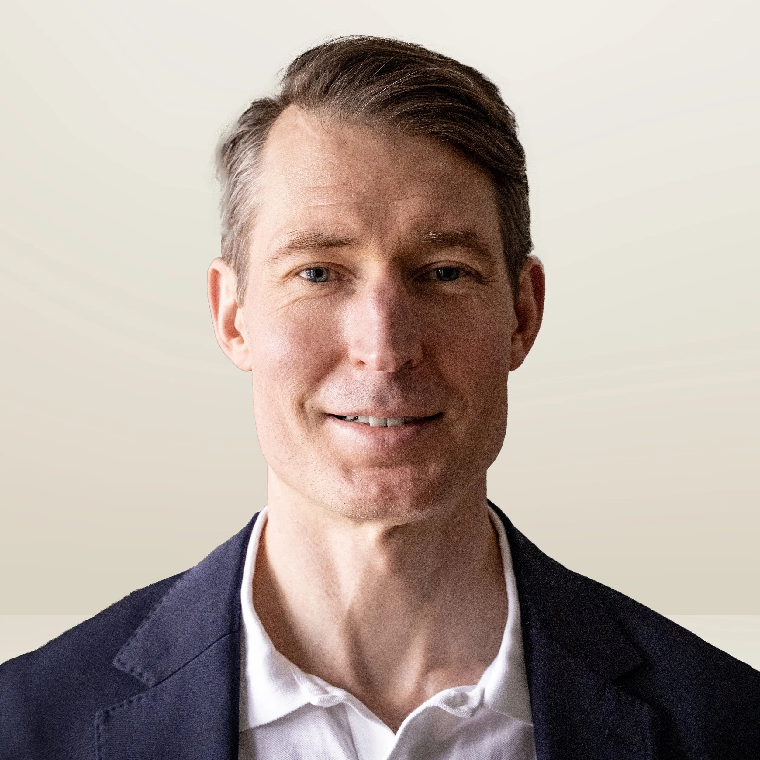 A young man with brown hair, wearing glasses and a dark jacket, standing against a plain light-colored background.