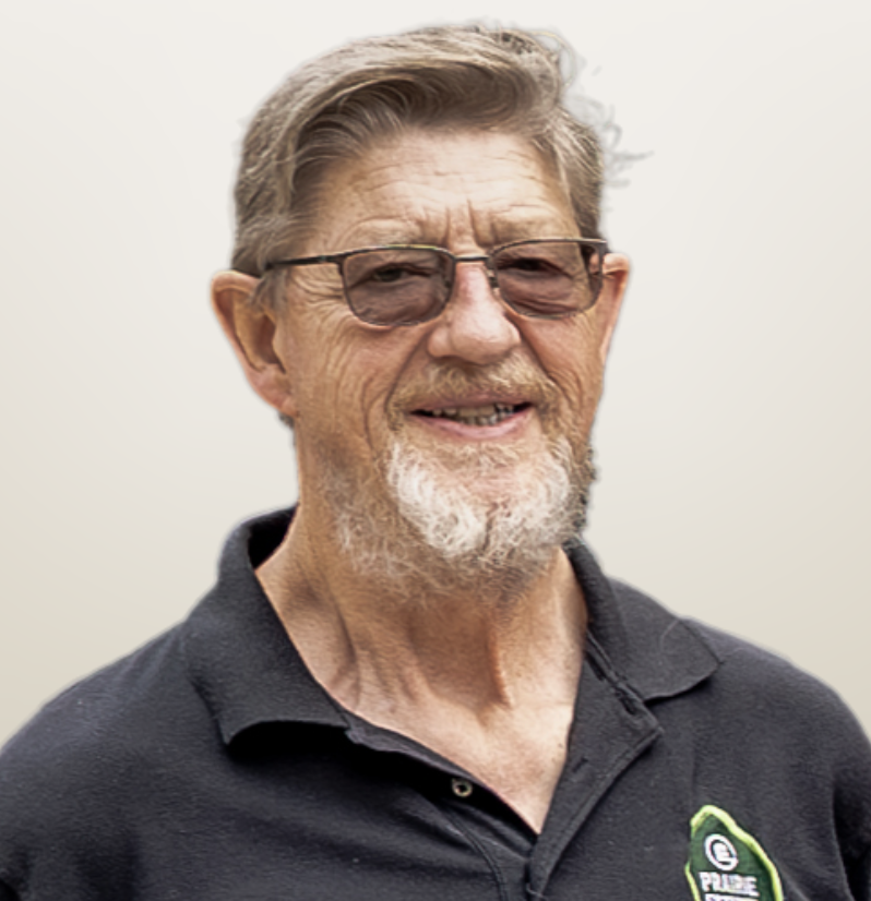 Older man with glasses and gray hair, wearing a black collared shirt with a logo, smiling against a plain background.