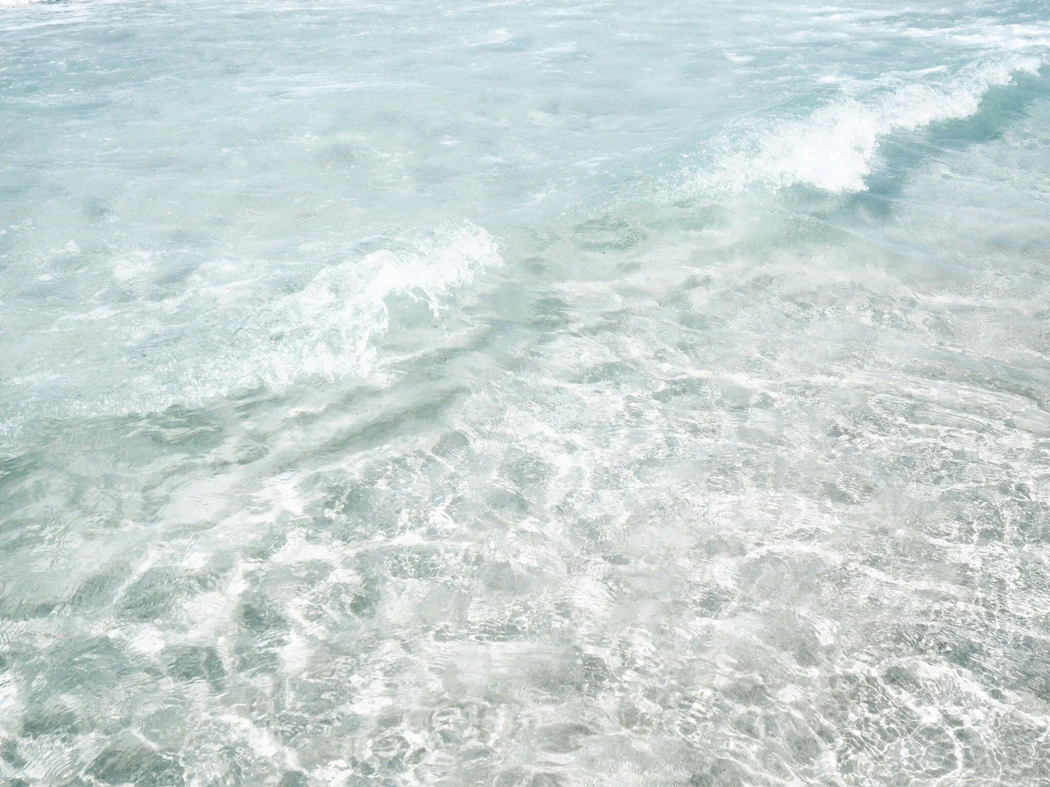 Close-up of a gentle shoreline with clear ocean water, small waves, and a sandy seabed