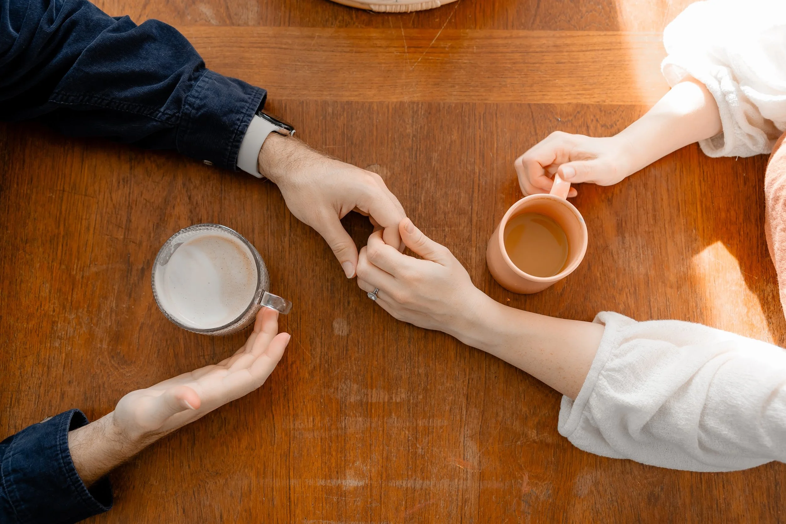 Two people holding hands on a table, with one person placing their hand on top of the other's.