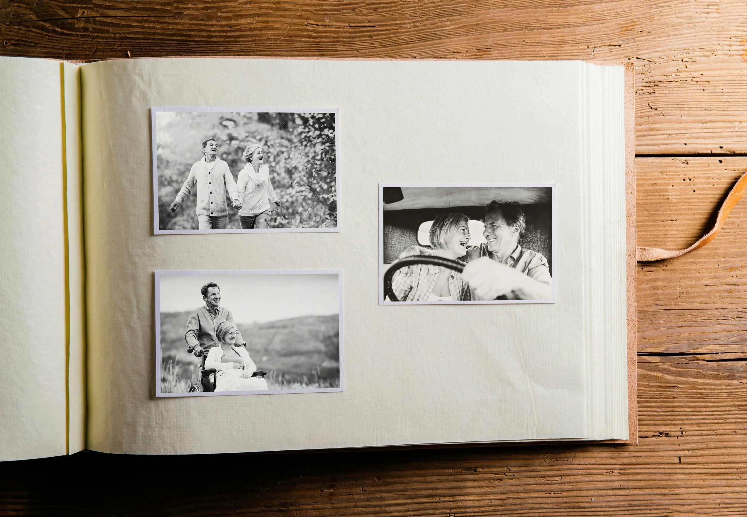 A scrapbook open to pages with three black and white photographs of people enjoying outdoor activities, on a wooden surface.