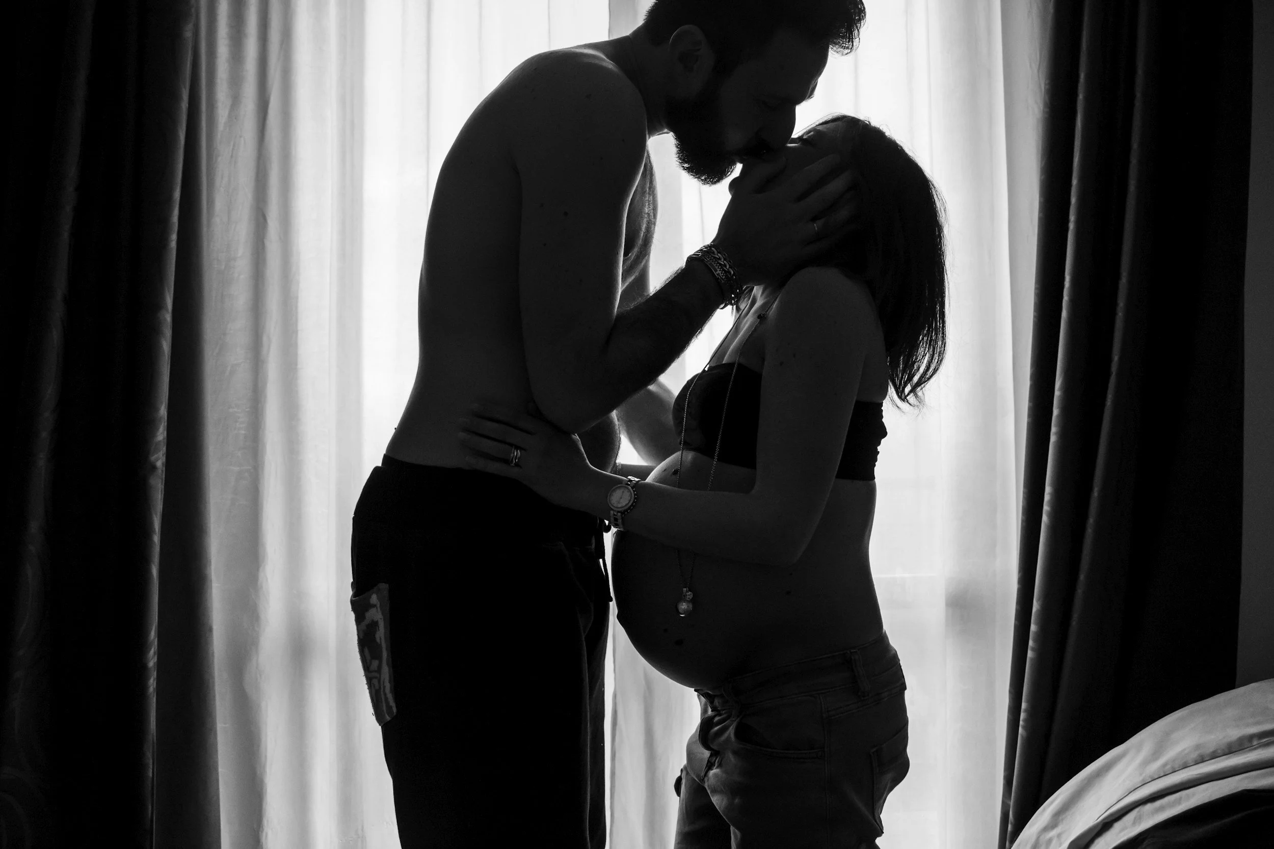 Silhouettes of a man and a woman close together, with the man touching the woman's face, in front of a backlit curtain.