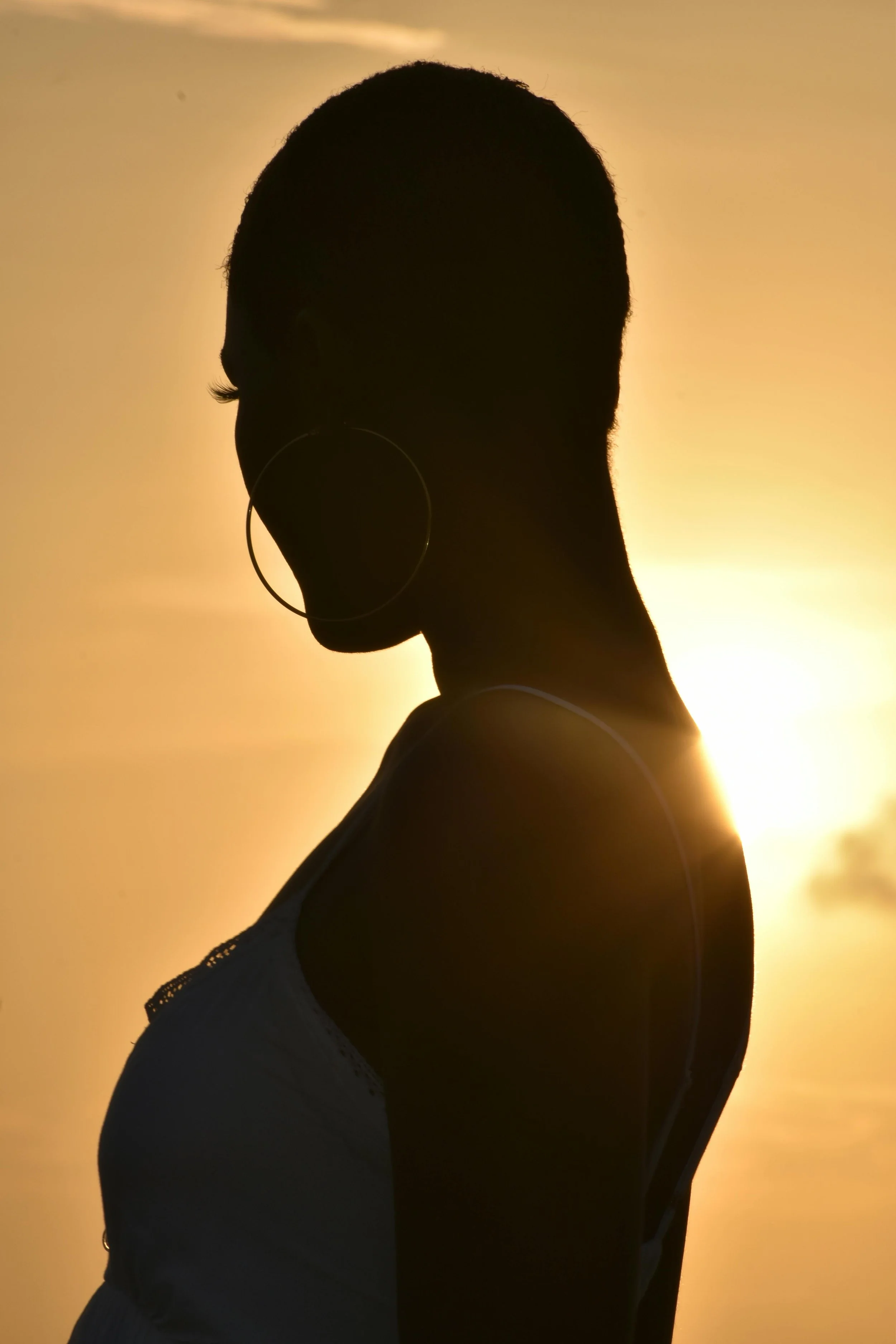 Silhouette of a woman with a short haircut and hoop earrings, standing against a sunset sky.