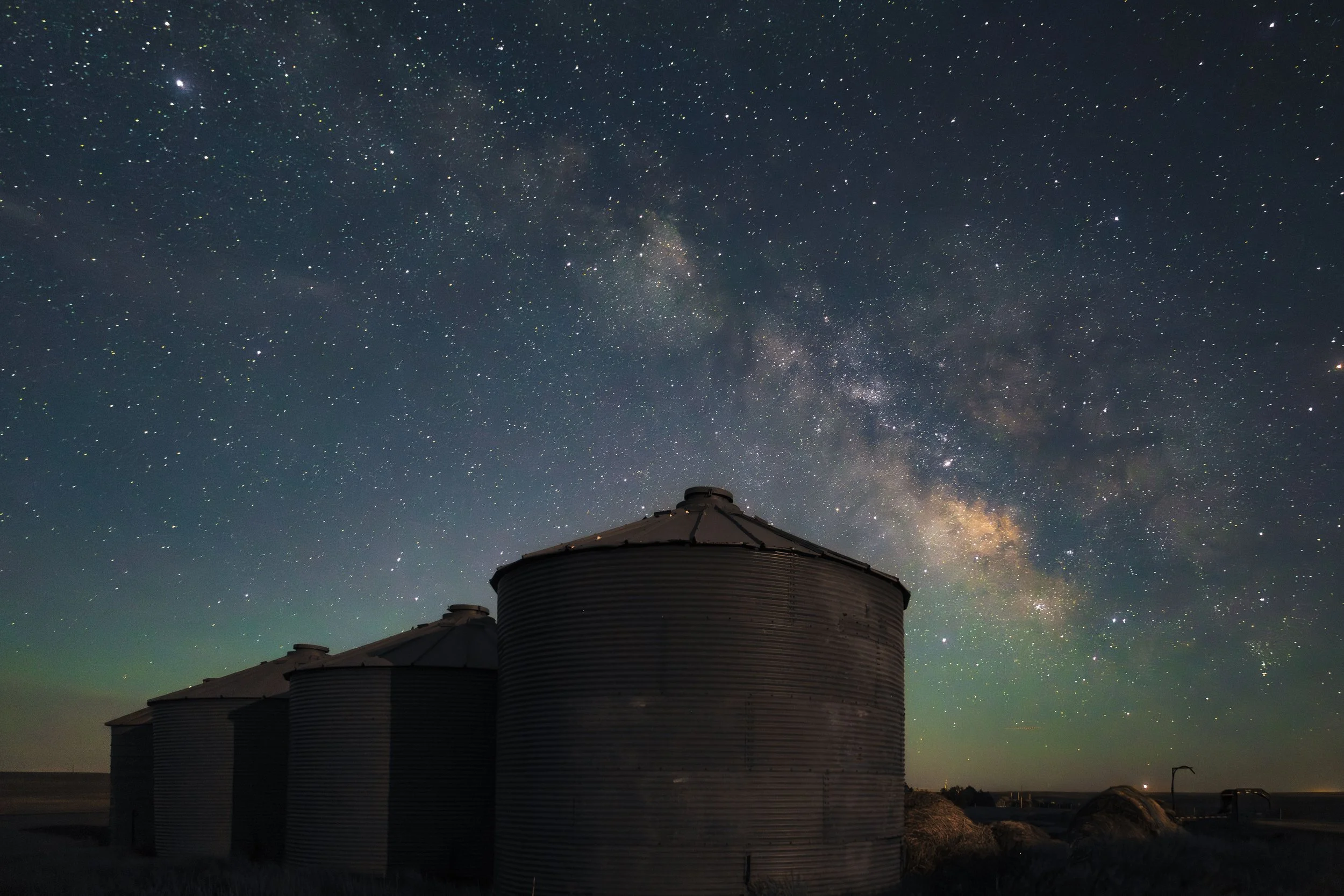 Silhouettes of grain silos under a star-filled night sky with the Milky Way galaxy visible.