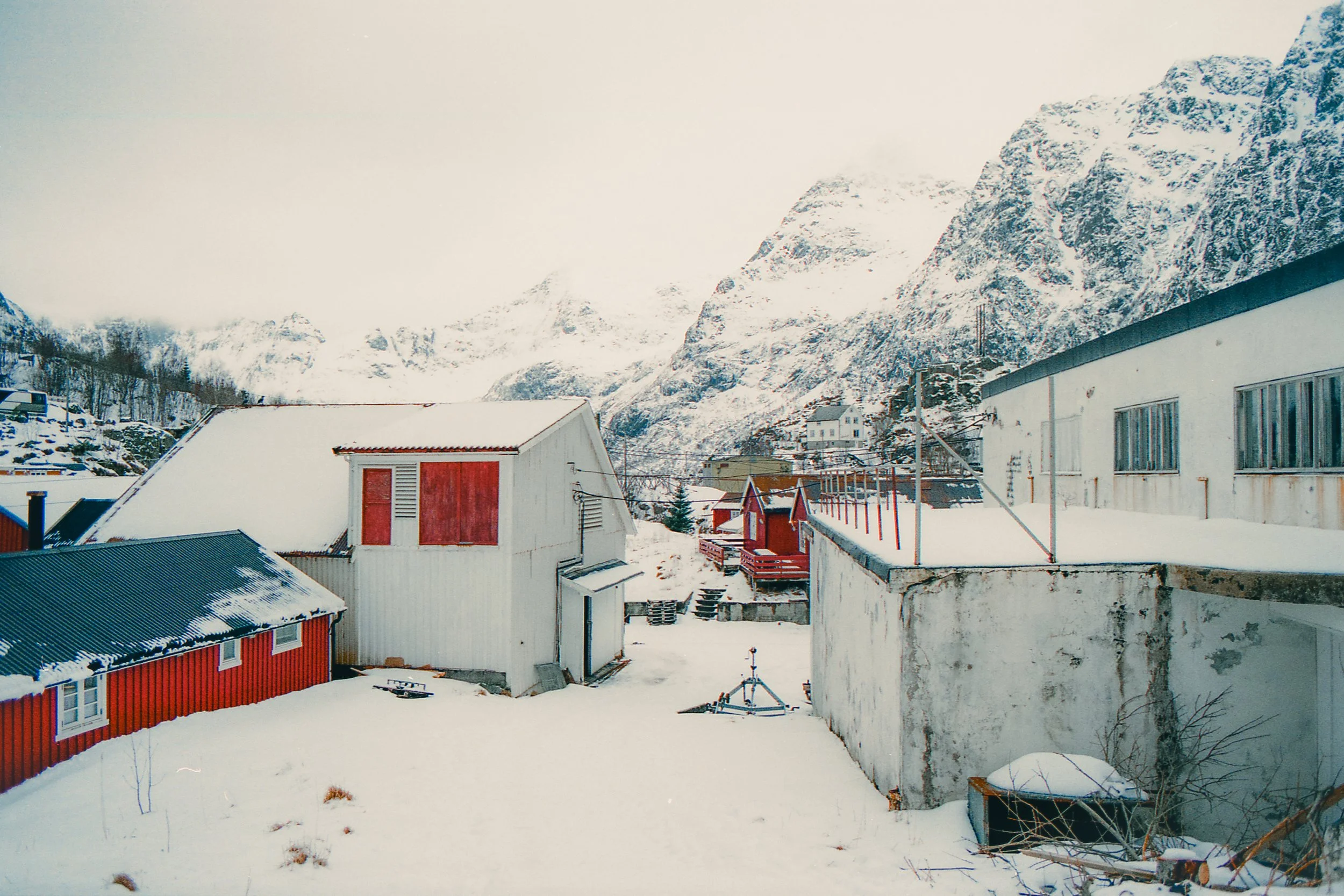 Snow-covered buildings in a mountainous landscape with snow-capped peaks in the background.