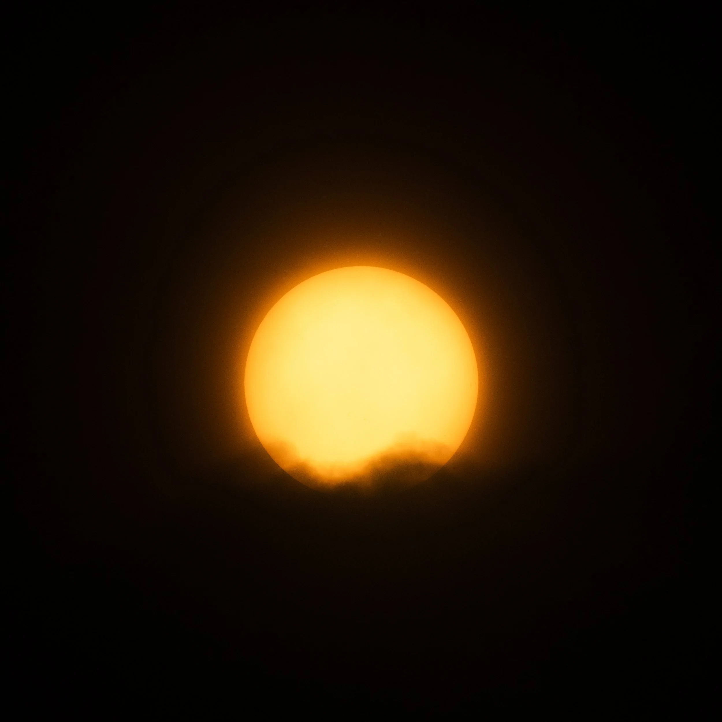 The sun partially obscured by clouds, glowing brightly against a dark sky.