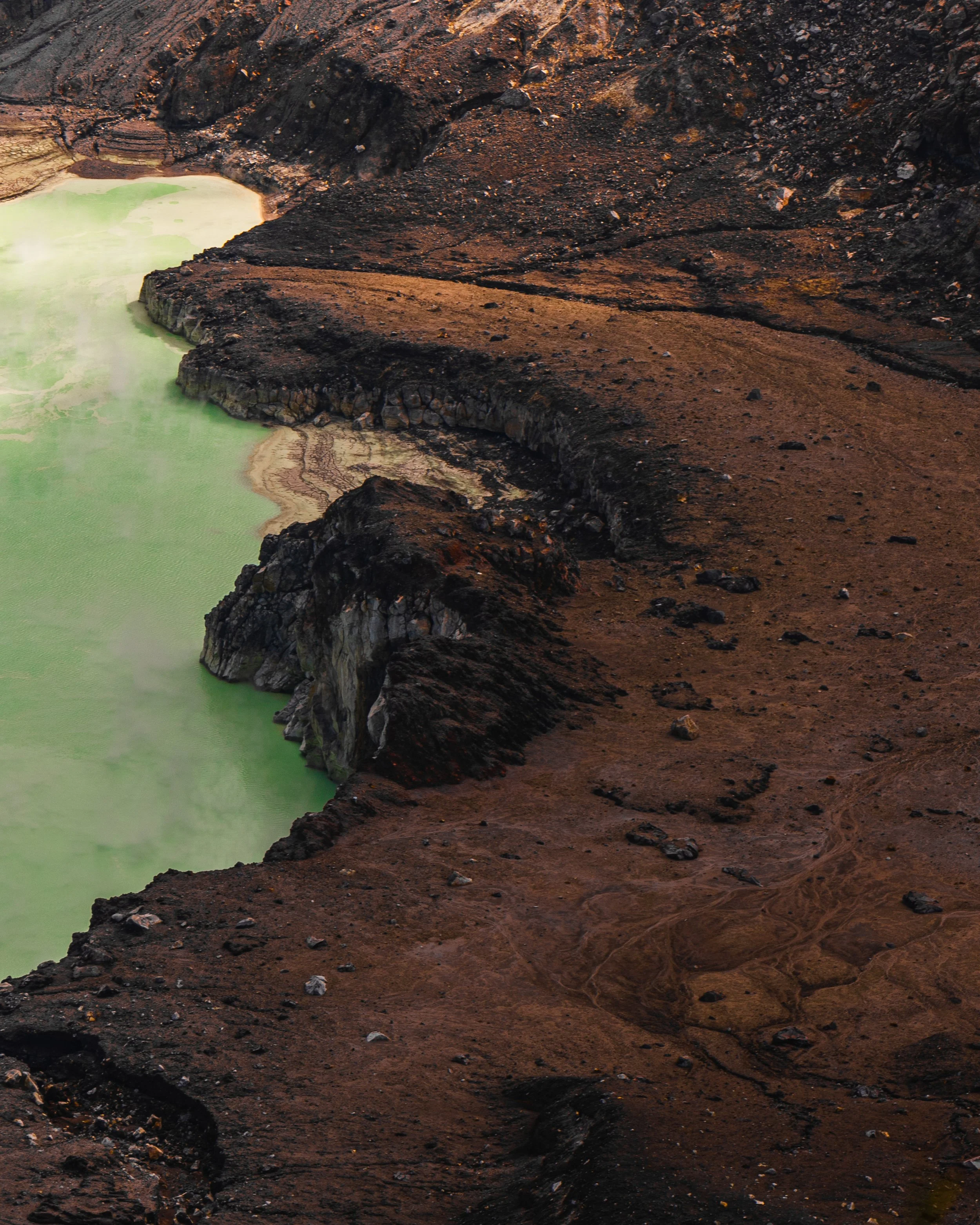 A volcanic landscape with brown, rocky terrain and a greenish geothermal hot spring or lake.