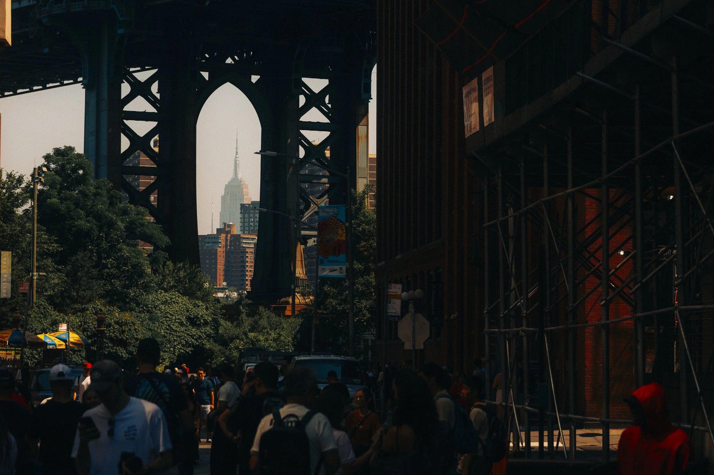 People walking under an elevated train track with the Empire State Building in the background in New York City.