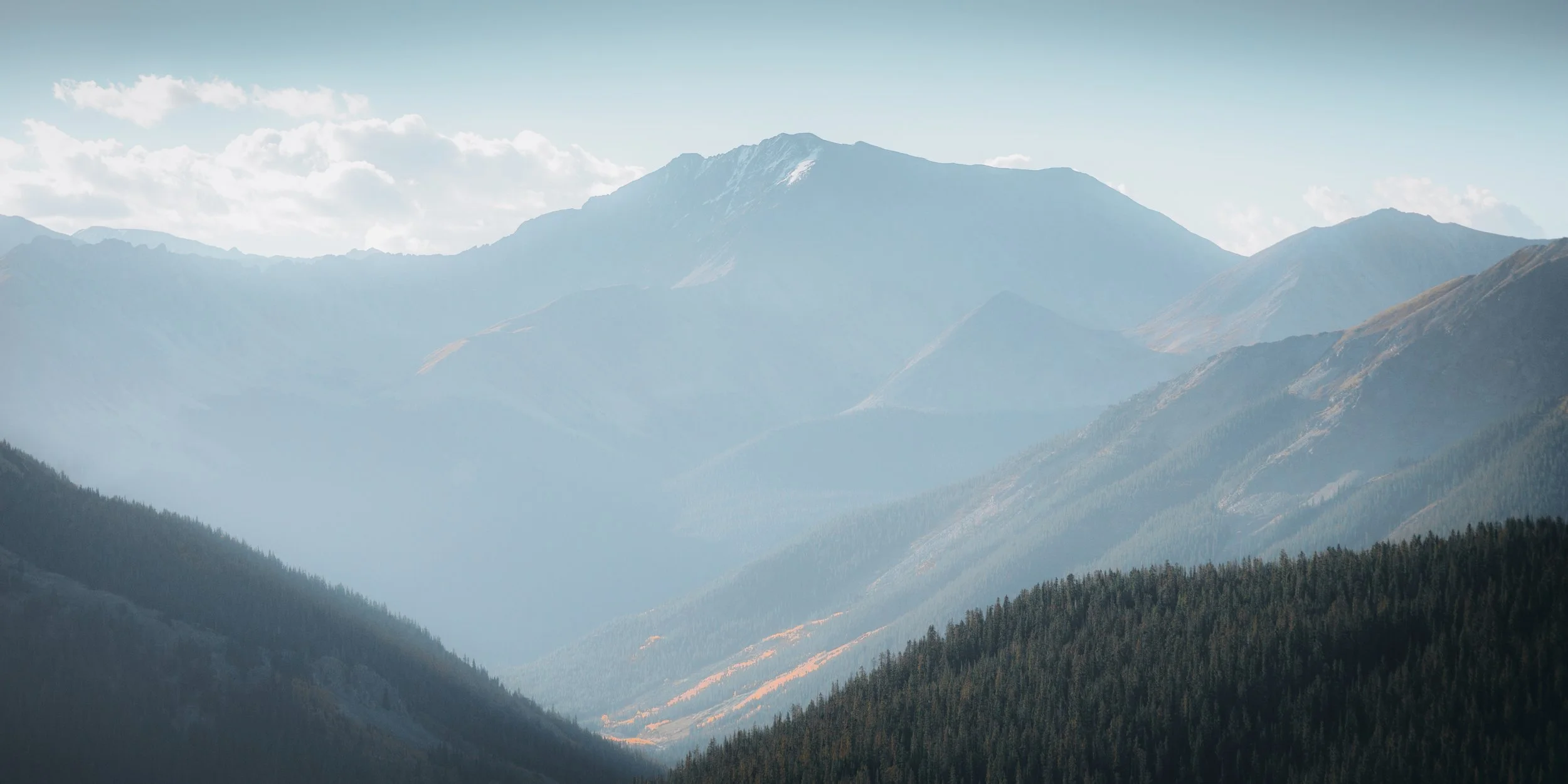 Scenic view of blue mountain ranges with forested slopes and clouds overhead.