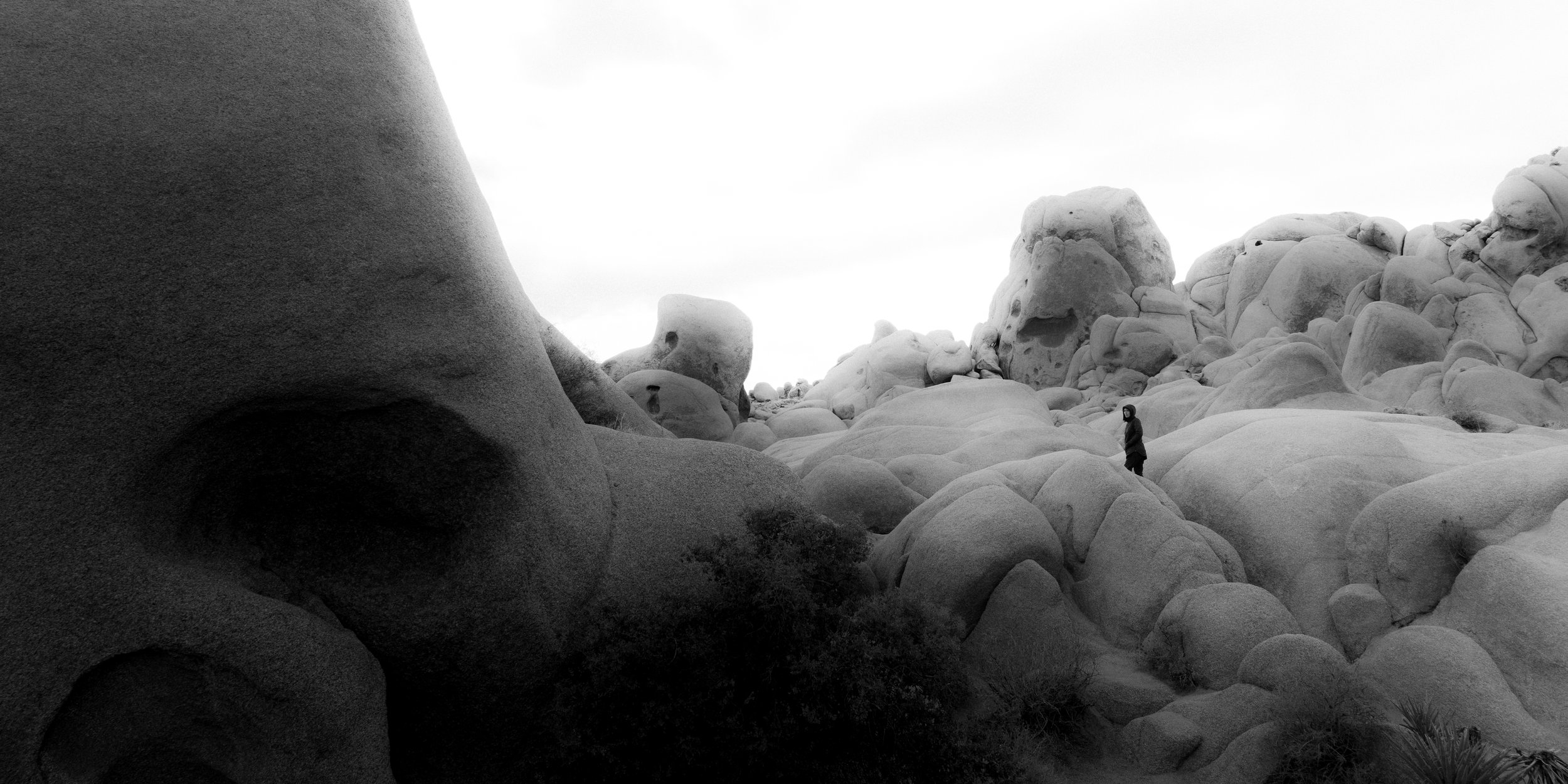 A person standing among large, rounded boulders in a desert-like landscape with a cloudy sky.