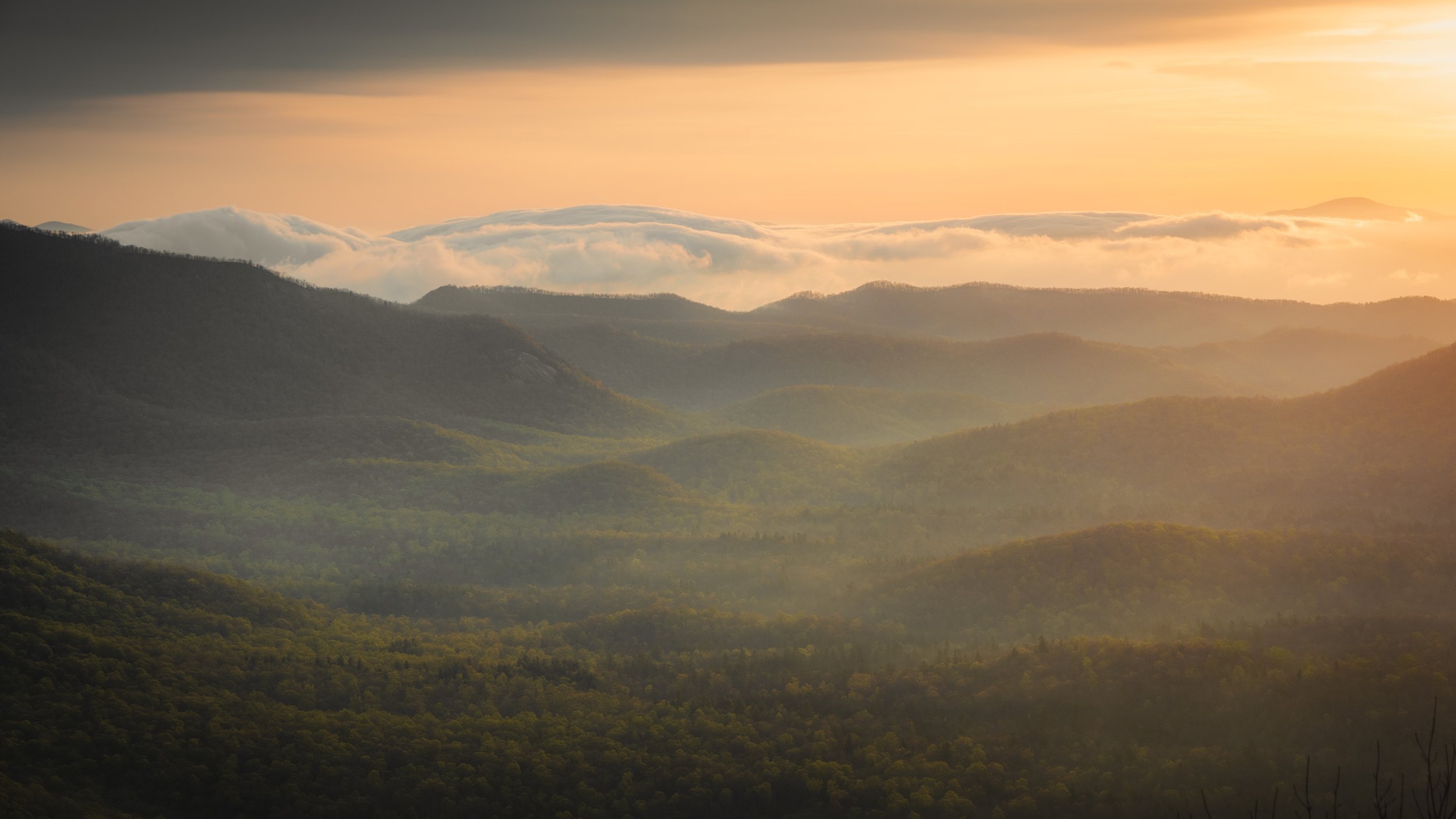 Sunset over rolling green mountains with clouds in the sky.