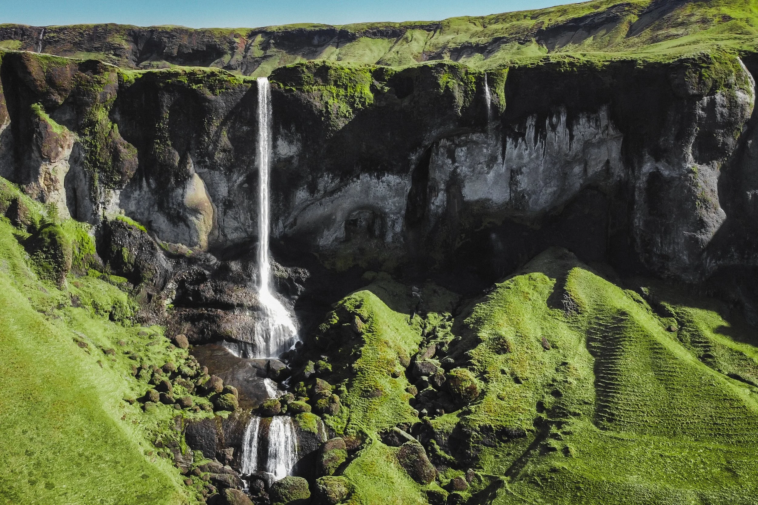 Green grassy hills with a tall waterfall cascading down dark rocky cliffs.