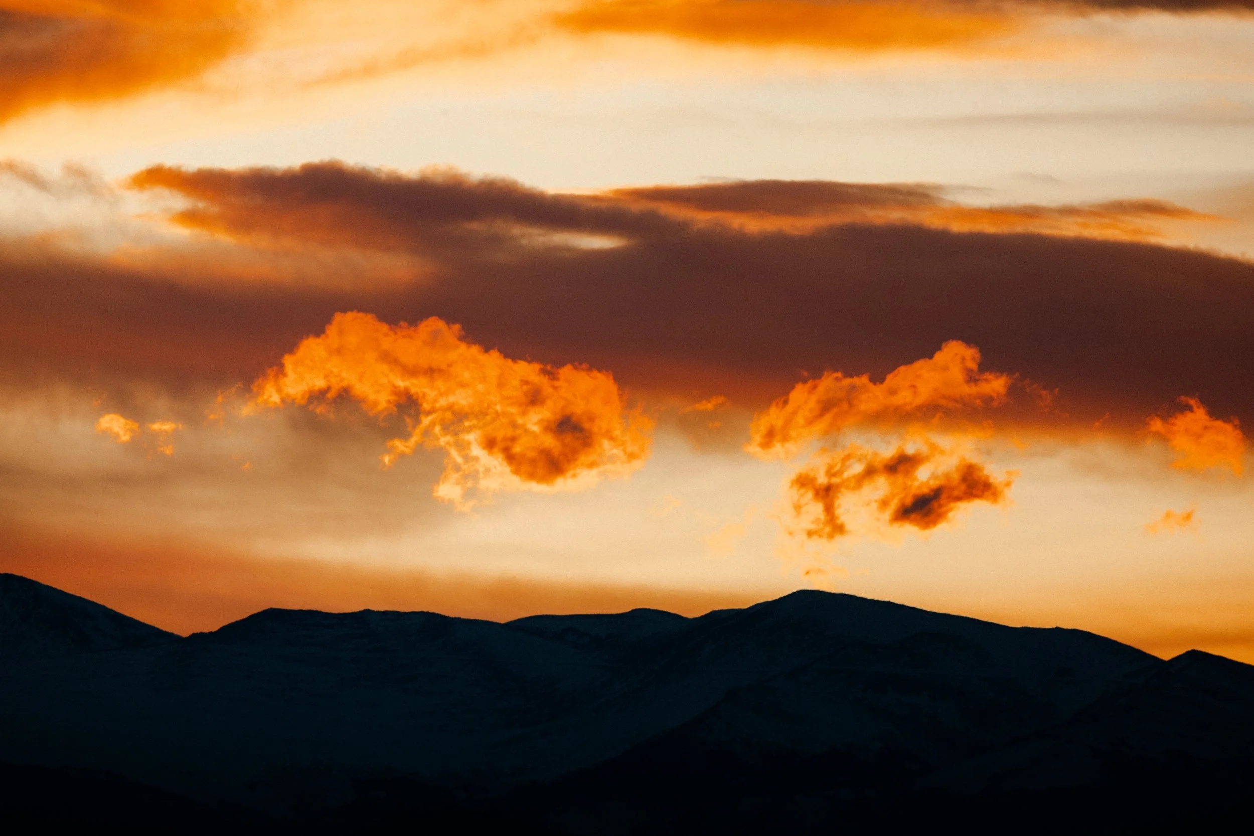 Sunset over mountain silhouette with orange clouds in the sky.