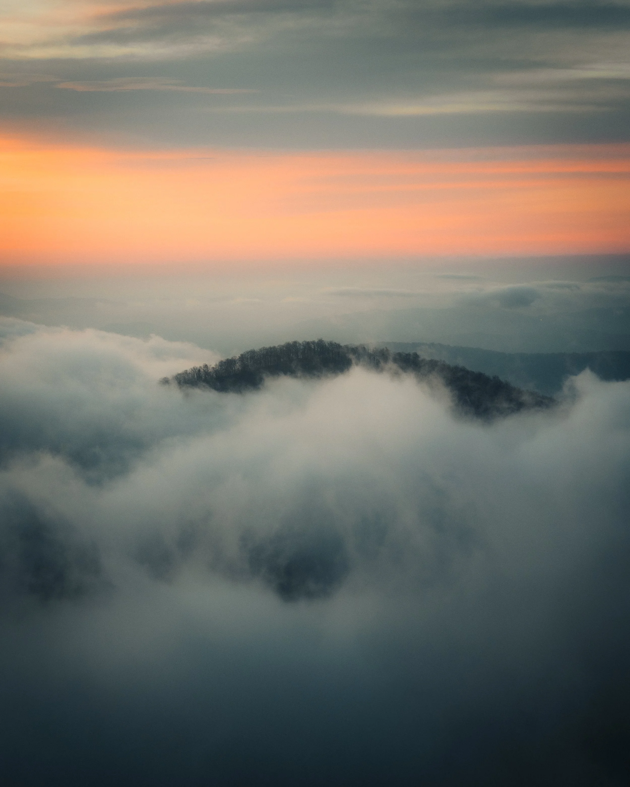 A mountain peak surrounded by clouds with a colorful sunset sky in the background.