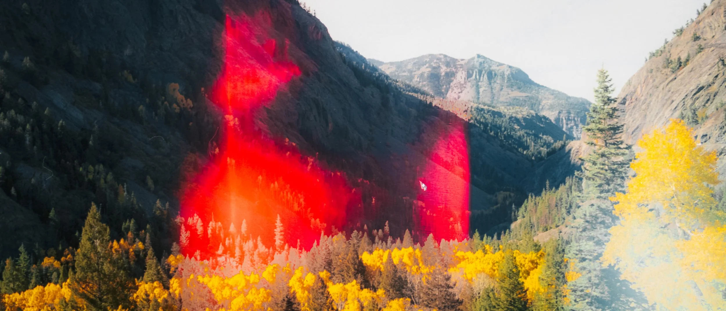 Forest in a valley surrounded by mountains with a large red fire on the hillside.