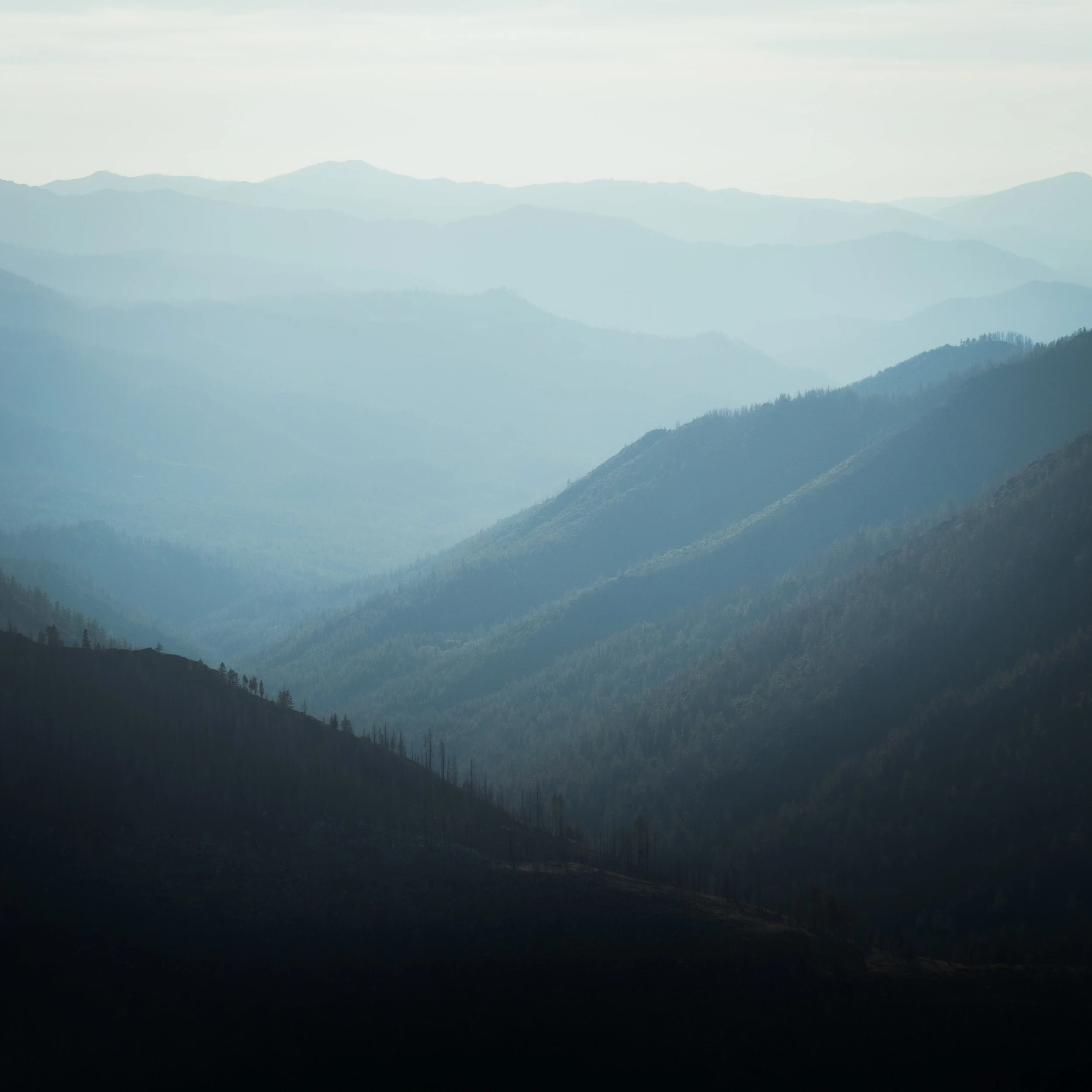 A scenic view of multiple mountain ranges with layered, misty blue peaks extending into the distance.