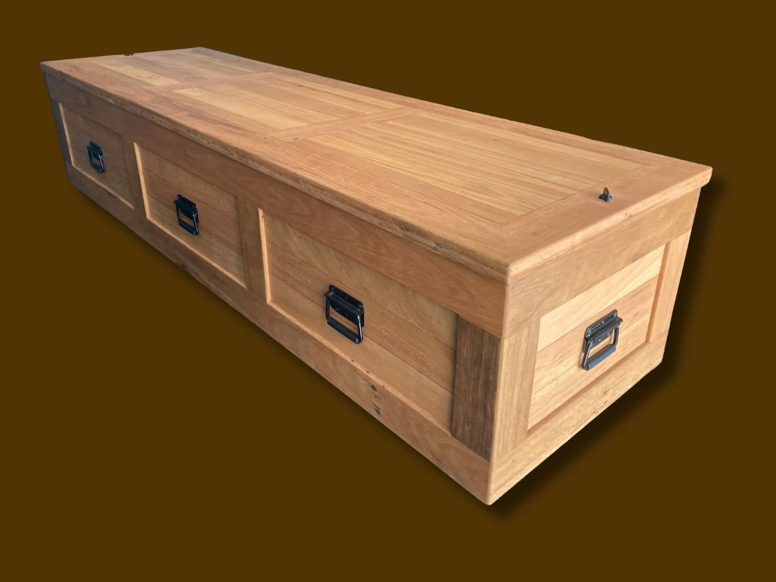 Warath casket from top and side view, showing metal handles on the sides and a flat closed lid with a brown background. The casket is made from recycled Blackbutt timber and has a light stain