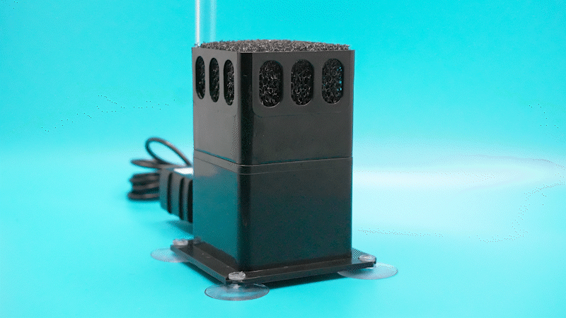 A black electronic device with multiple circular ventilation holes on top is mounted on a clear base with suction cups against a blue background.
