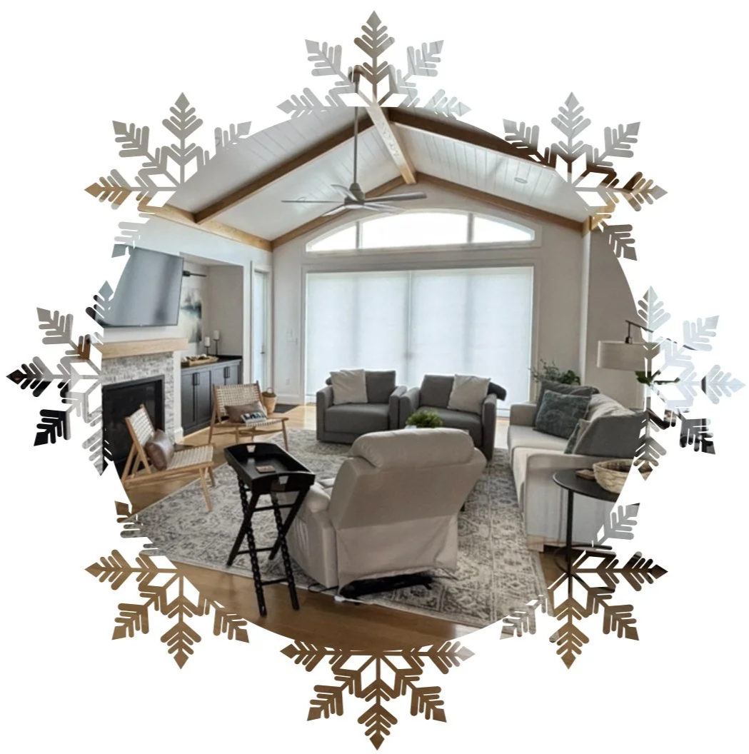 Bright living room with large windows, vaulted ceiling with ceiling fan, fireplace with TV above, and modern furniture including a sofa, chairs, and a rug, decorated for winter with a snowflake border overlay.