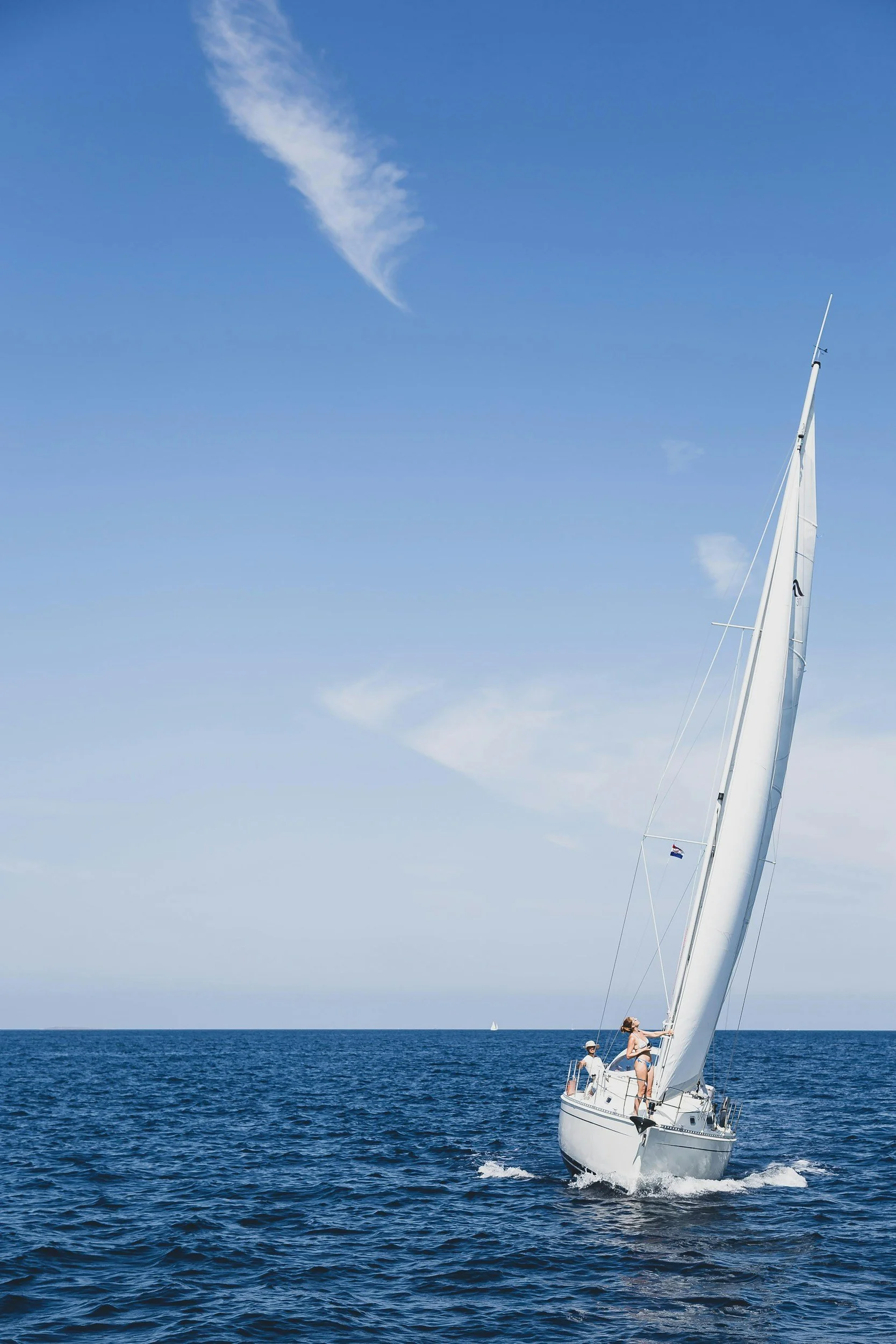 Sailboat on the ocean with blue sky and wispy clouds.
