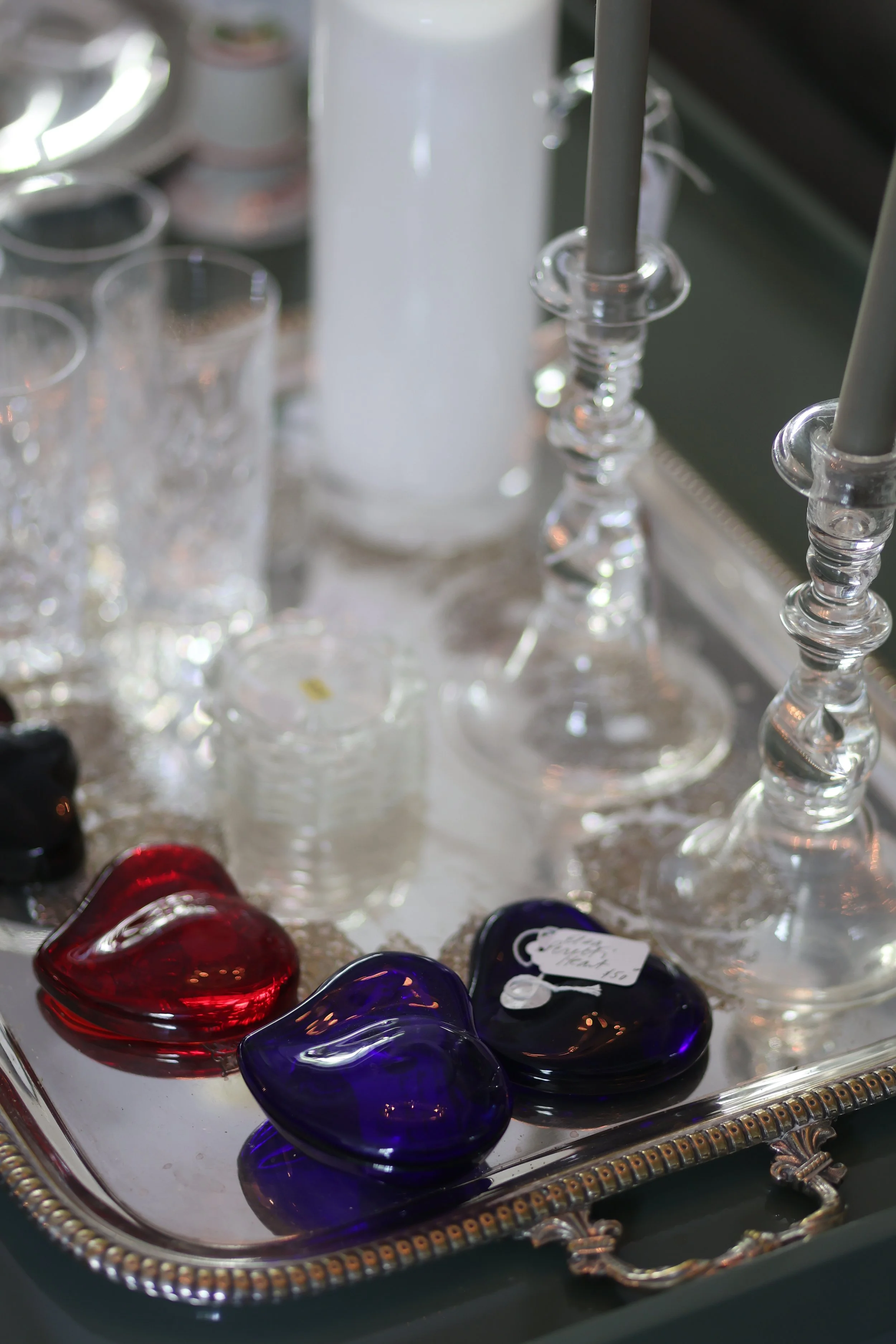 Glass display tray holding colorful glass hearts and two glass candle holders with gray candles.