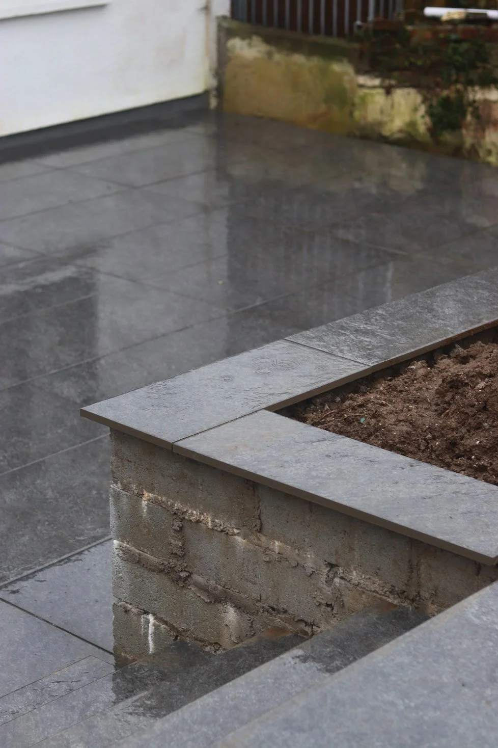 Newly laid porcelain patio with raised planter built by landscape contractors in Cornwall during wet weather conditions.