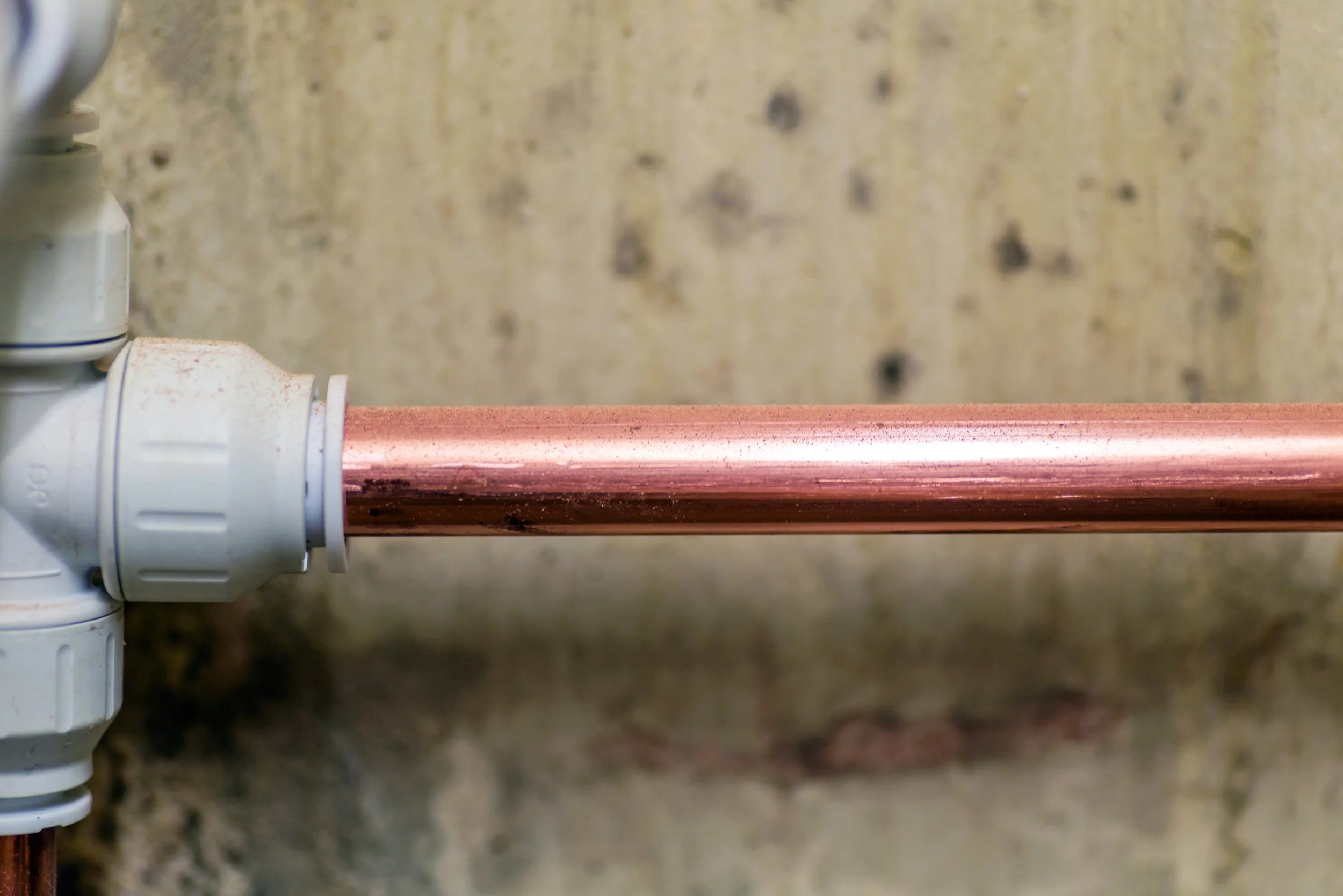Close-up of a copper pipe with plastic fittings attached, against a concrete background.