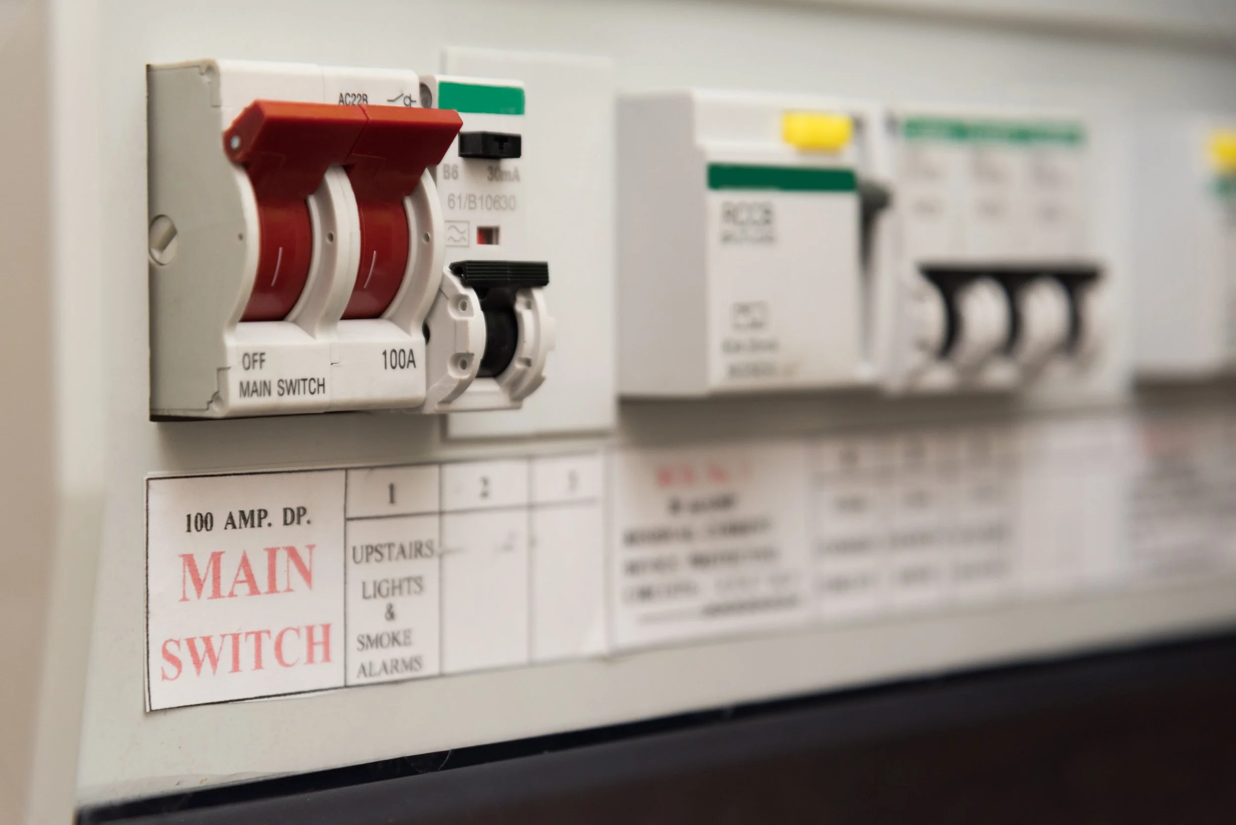 Close-up of an electrical breaker panel with red switches labeled 'Main Switch,' showing 100 AMP capacity and labels for different circuits.