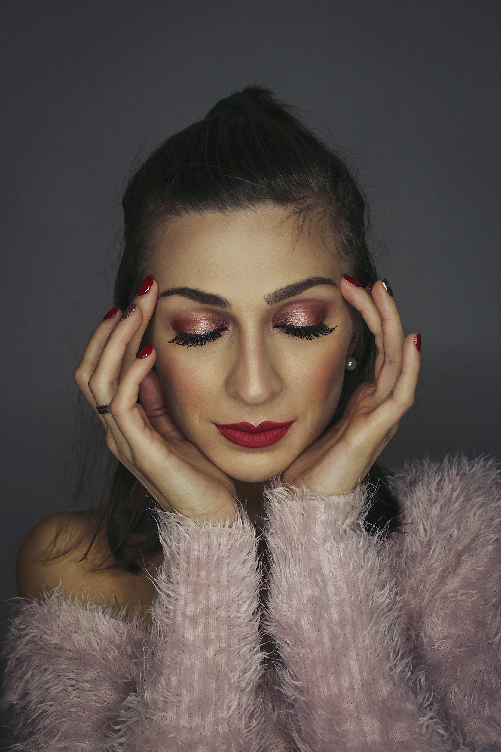 Nahaufnahme eines Gesichts mit dramatischem Make-up, langen schwarzen Wimpern und schwarzen Lippen vor rotem Hintergrund.