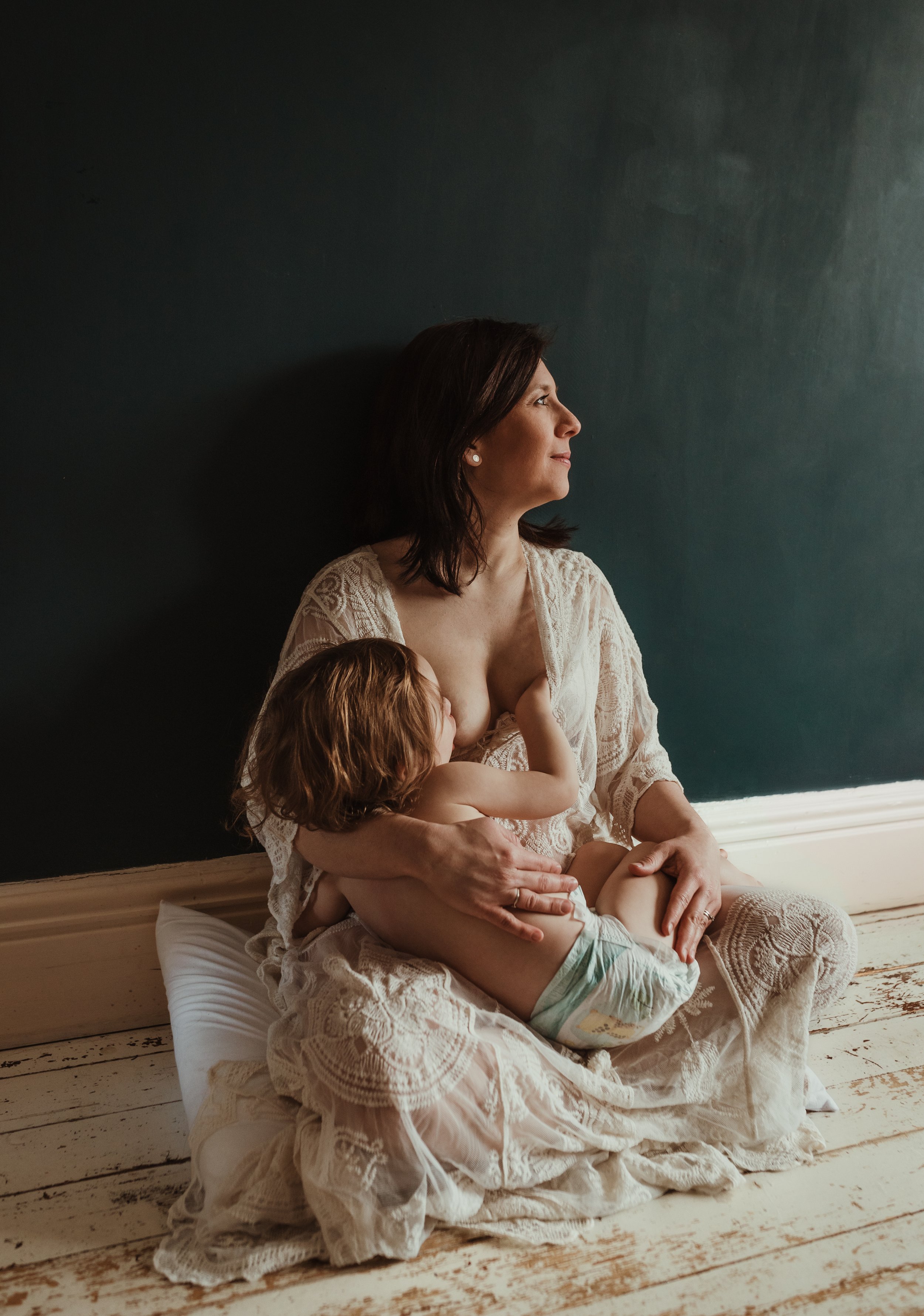 Mother nursing her toddler in a white lace dress indoors during a nursing photography session with Marieke Captures Birth Scotland