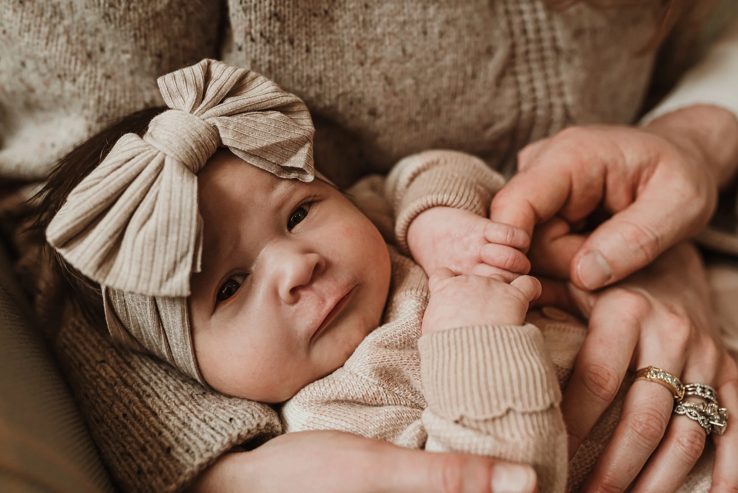 Newborn baby smiling with a bow headband held gently by mother's hands during a newborn photography session with Marieke Captures Birth Glasgow