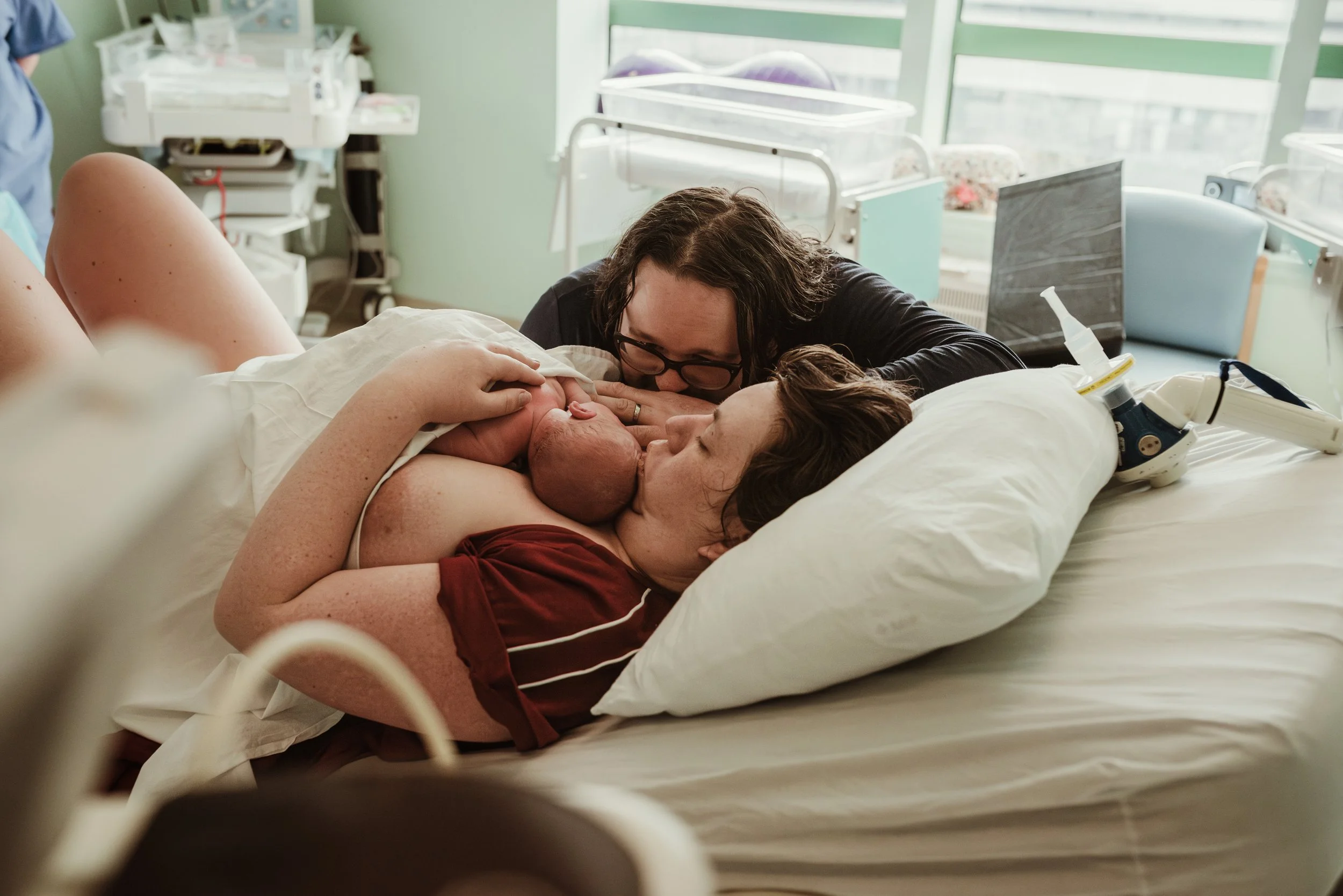 Mother kissing newborn on hospital bed, father beside them — hospital birth photography Glasgow, Marieke Captures Birth
