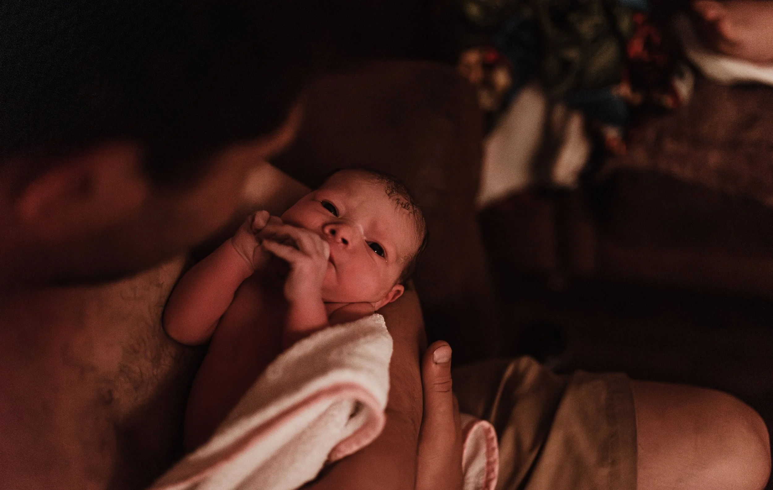 Father cradling his newborn in the golden hours after a home water birth in Ayr Scotland, wrapped in warmth and love