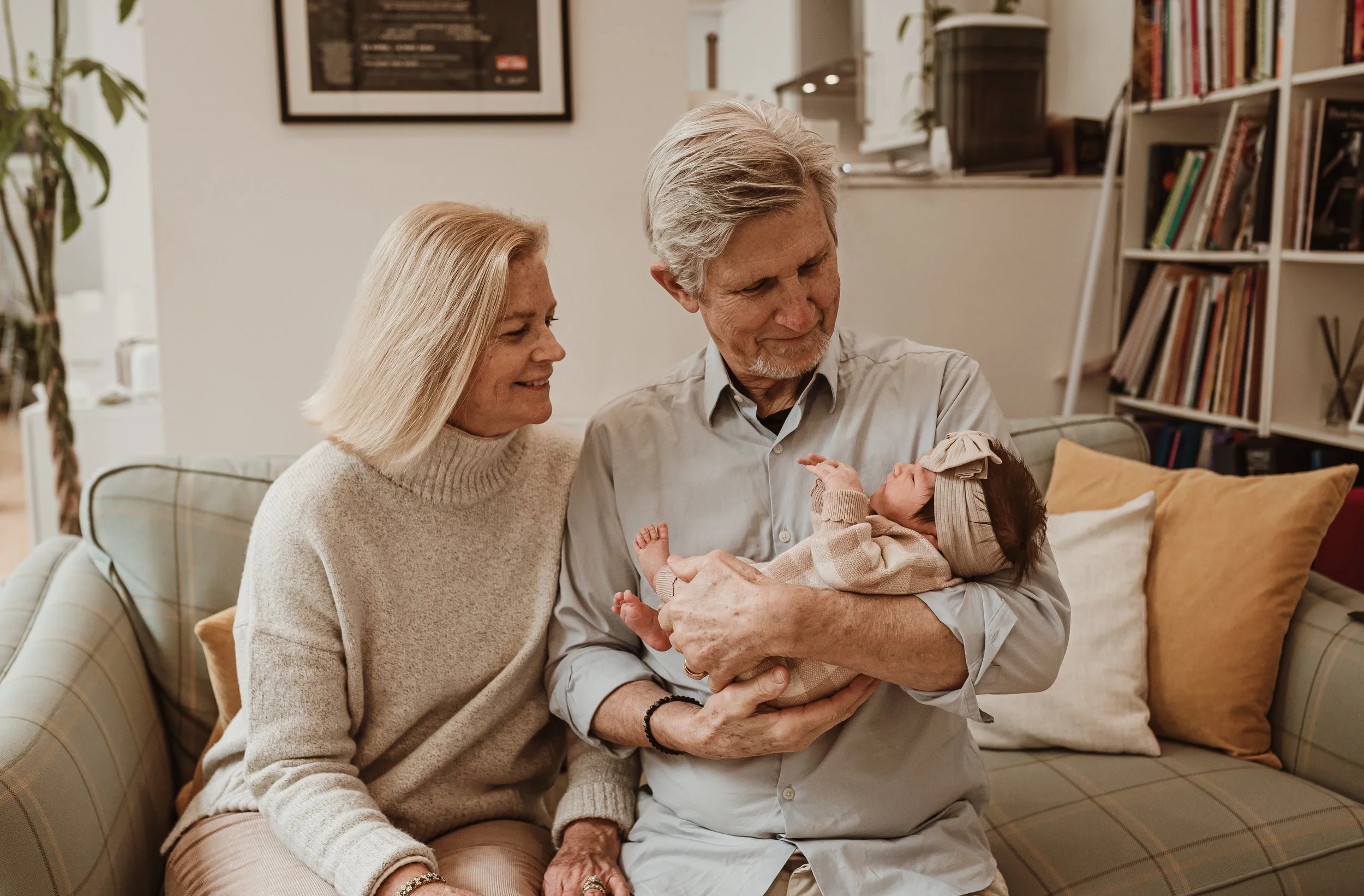 Grandparents sitting on a sofa holding their newborn grandchild during an at-home newborn photography session in Scotland with Marieke Captures Birth