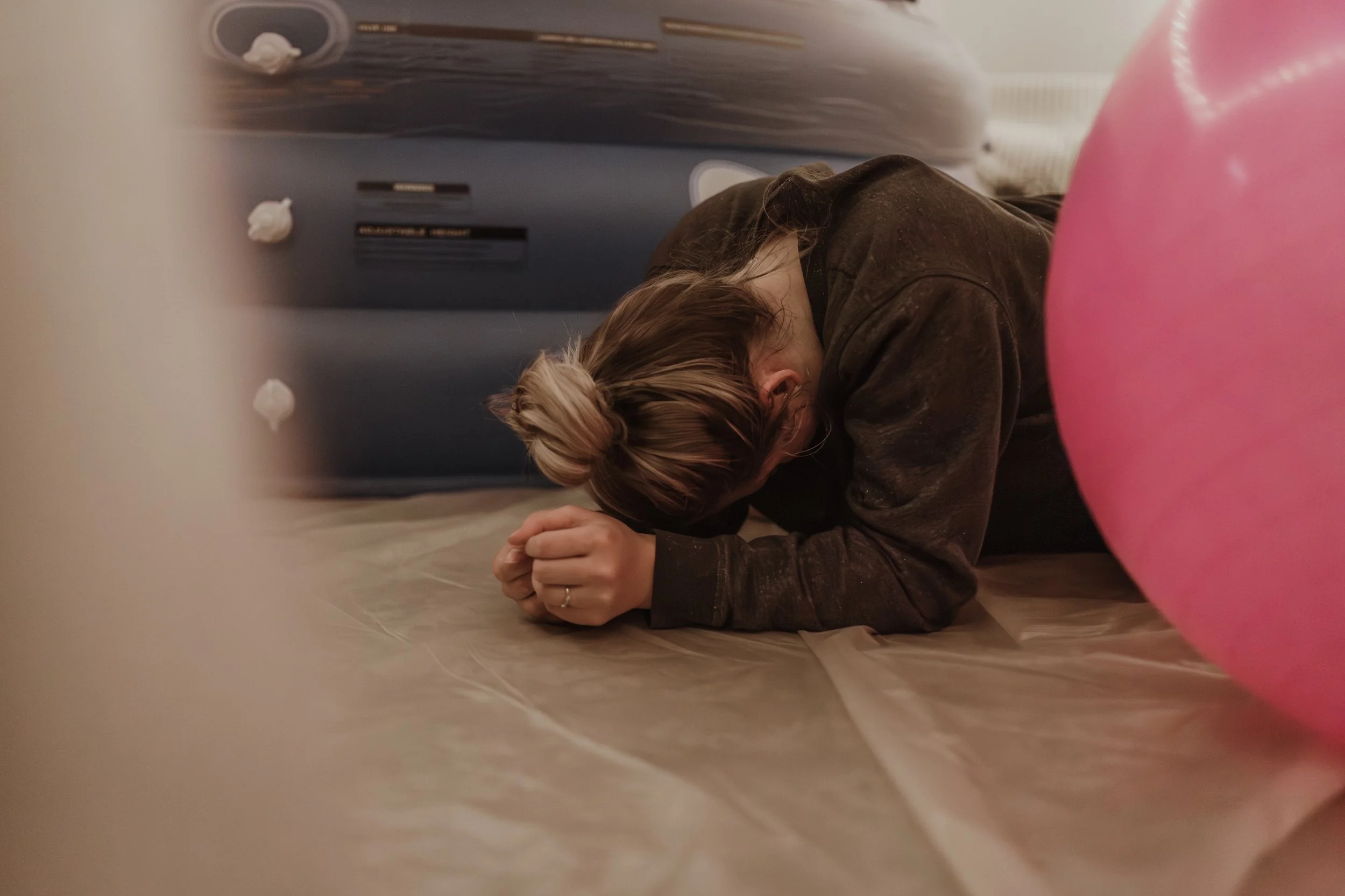 Rebekah hunched forward on the floor next to the birth pool during active labour at her Glasgow home birth, breathing through a powerful contraction